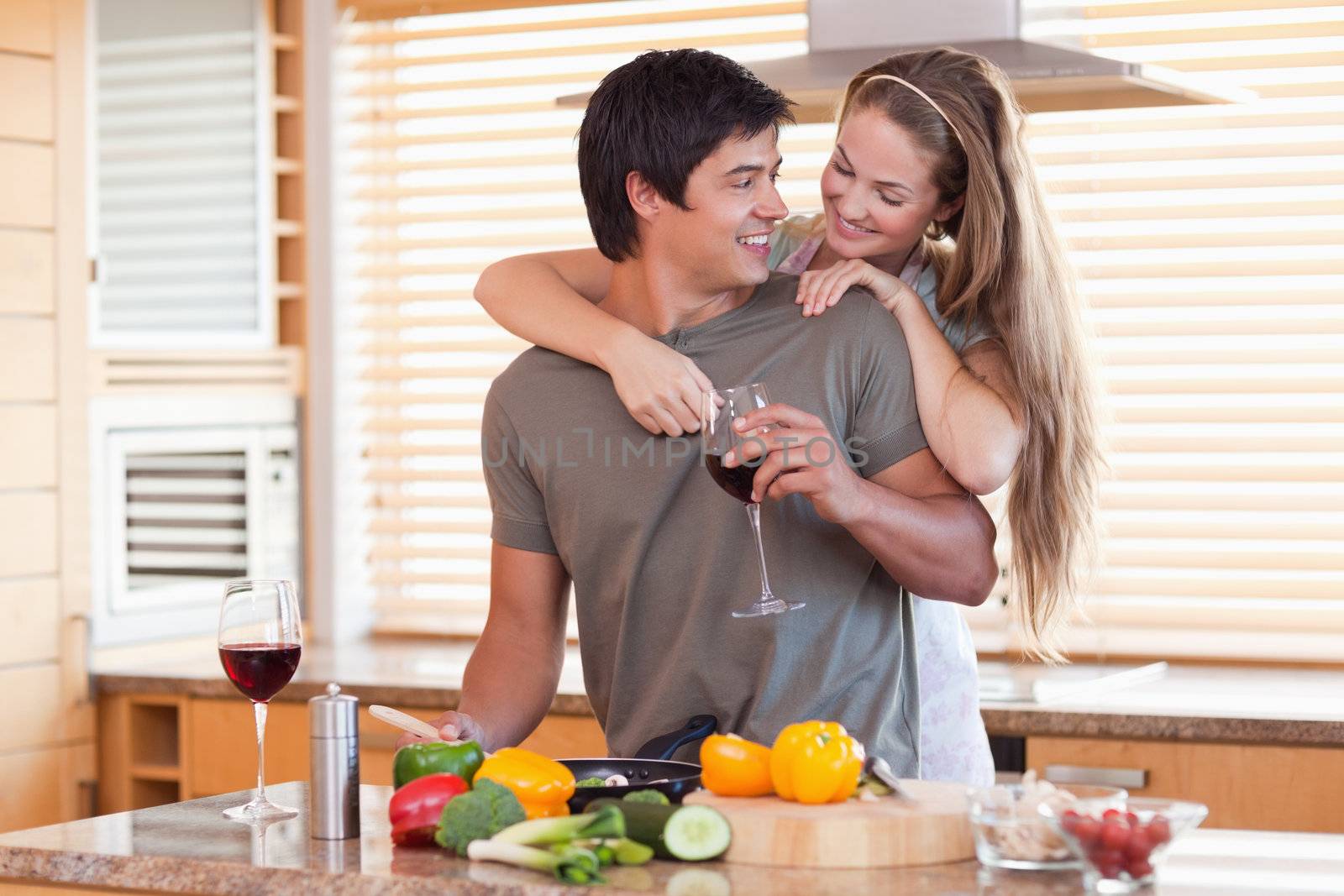 Lovely couple drinking wine while hugging in their kitchen