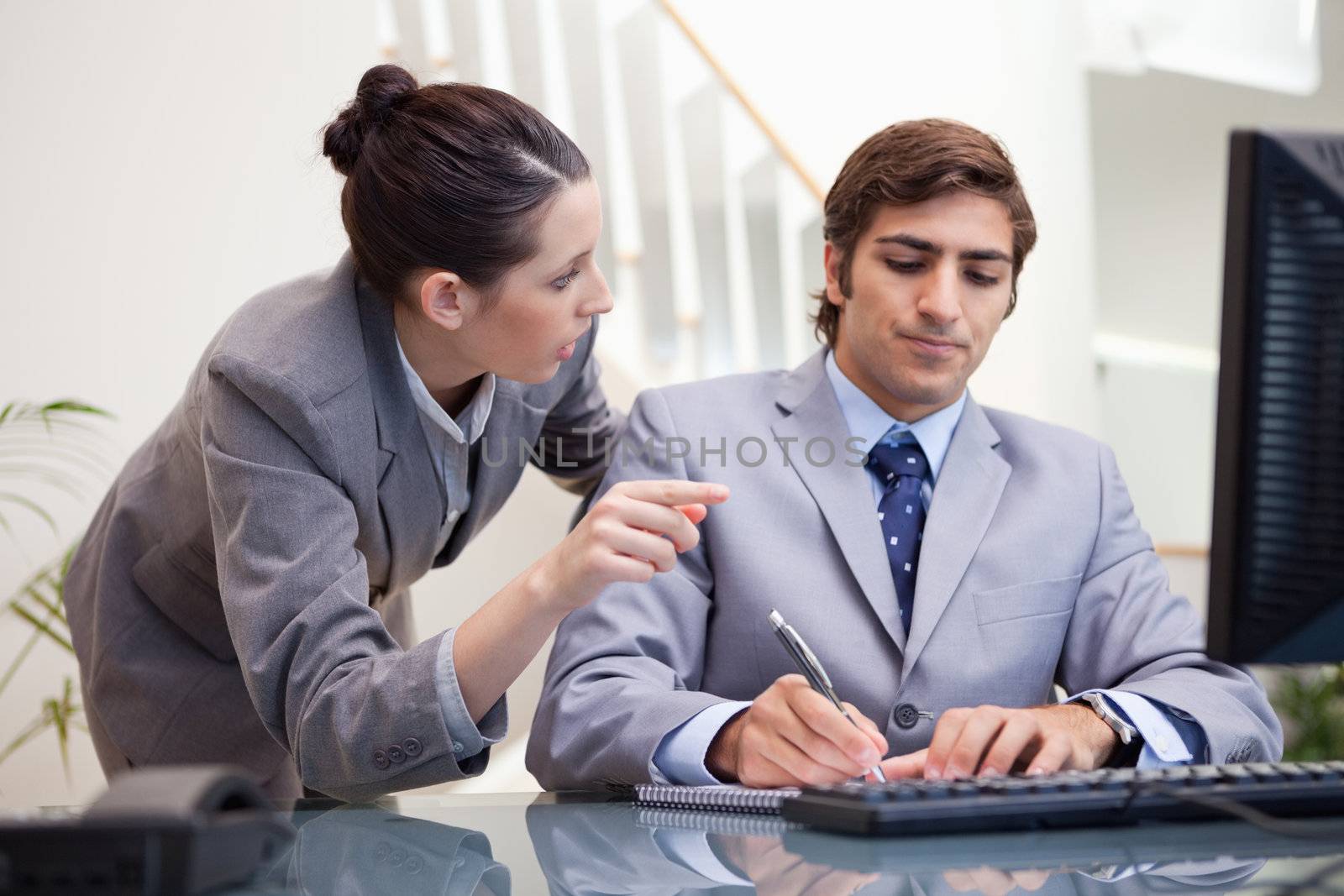 Young businessman taking notes while getting explanation by colleague