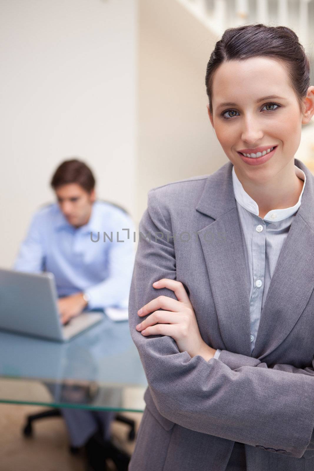 Smiling young businesswoman with colleague on his laptop behind her