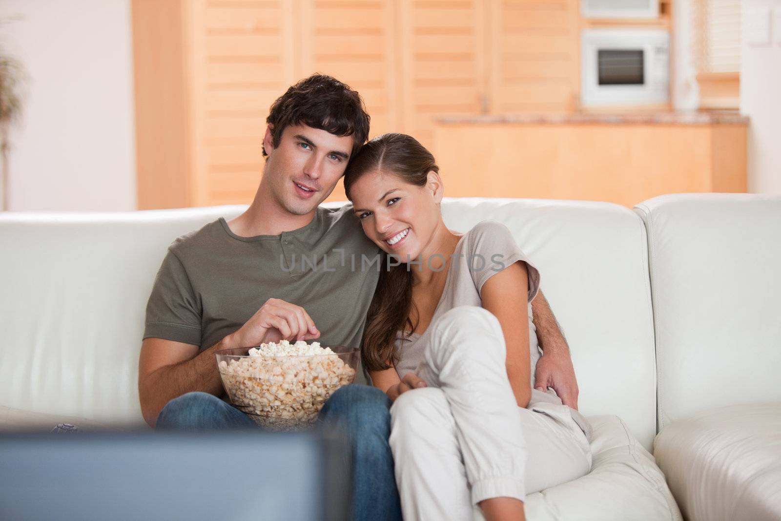 Young couple with bowl on popcorn watching a movie on the sofa