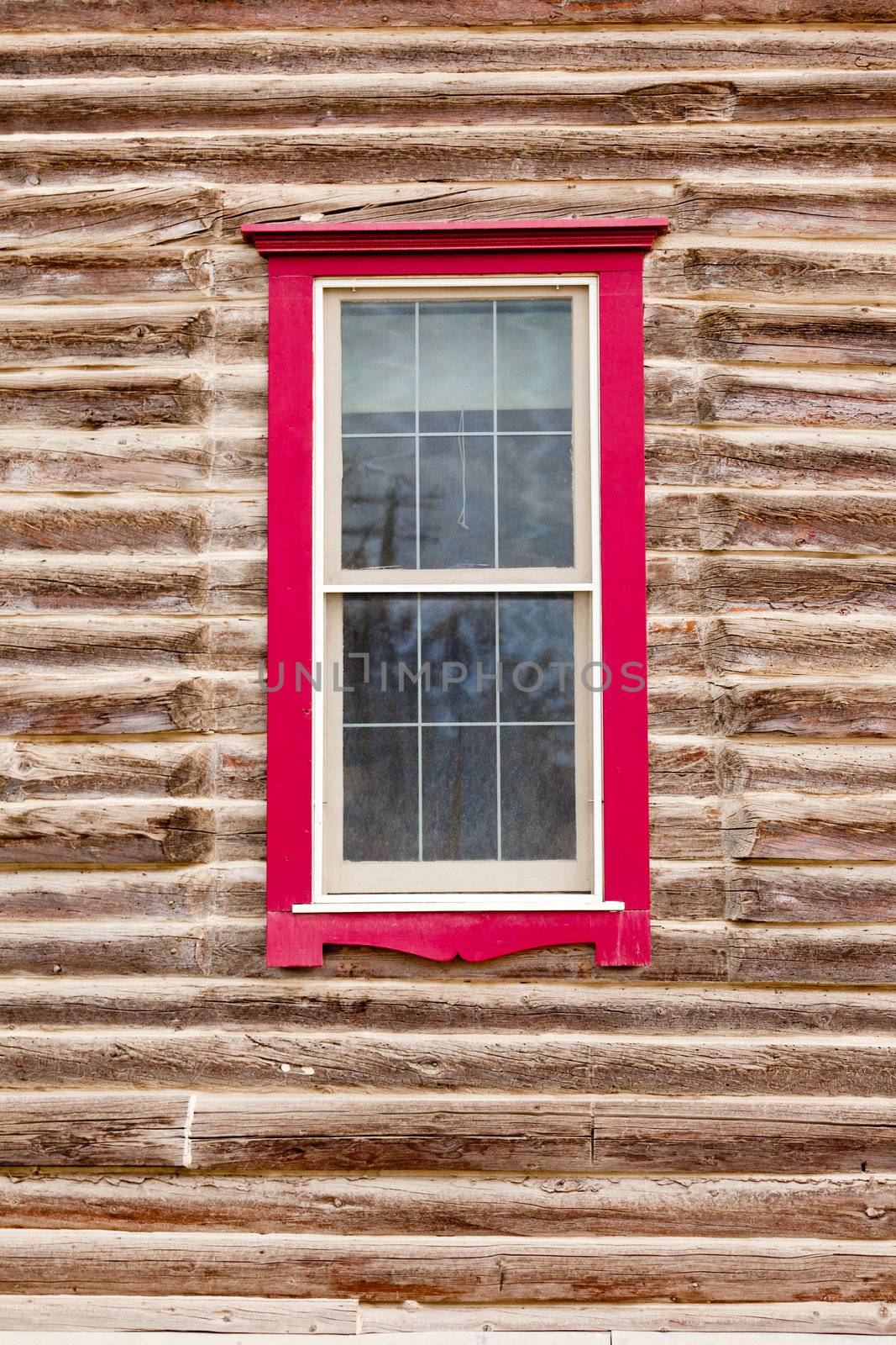 Architectural background of sash window with colourful red frame in exterior facade of a log building