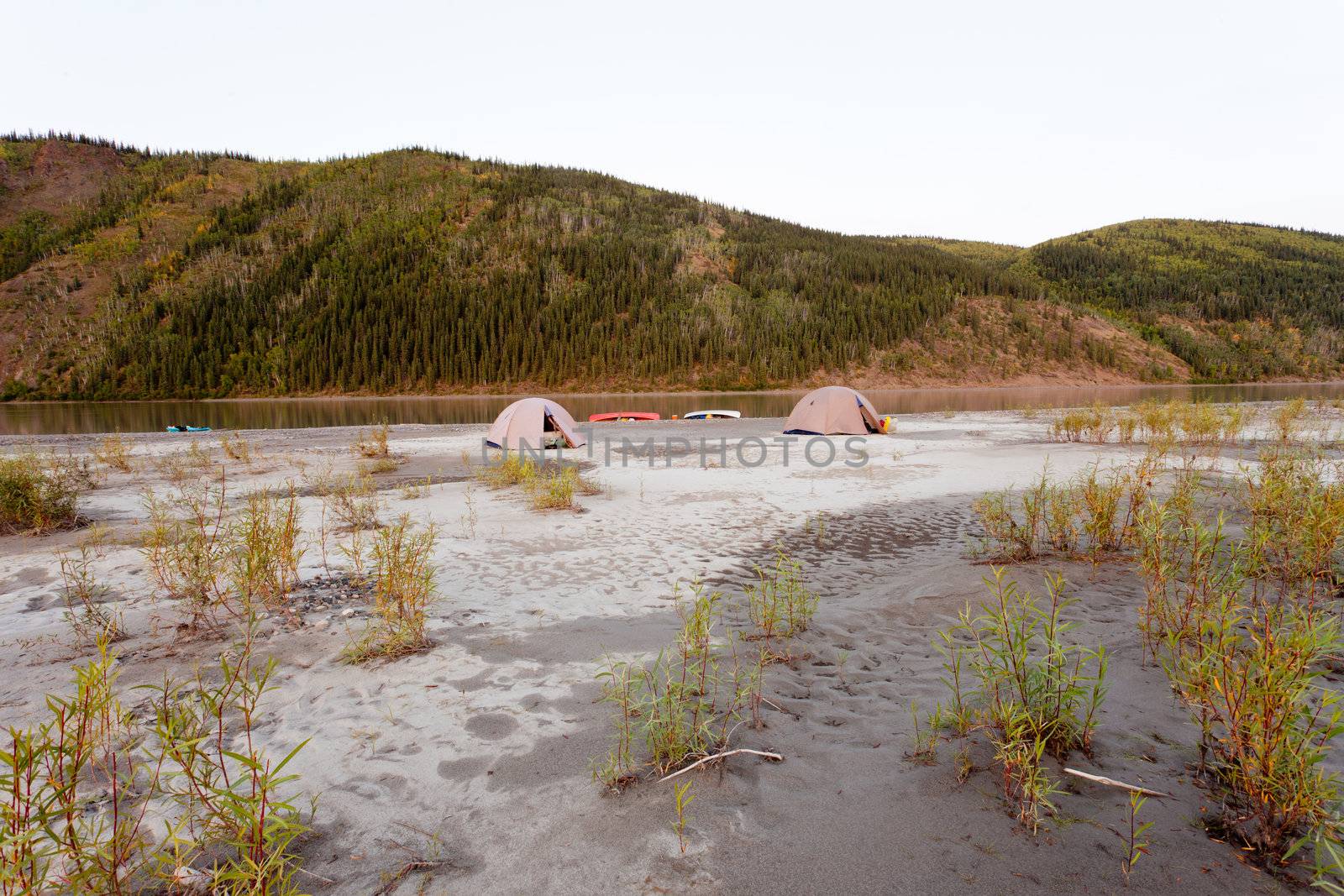 Beached canoes and two tents pitched on a sand bar alongside Yukon River, Yukon Territory, Canada, in remote boreal forest wilderness