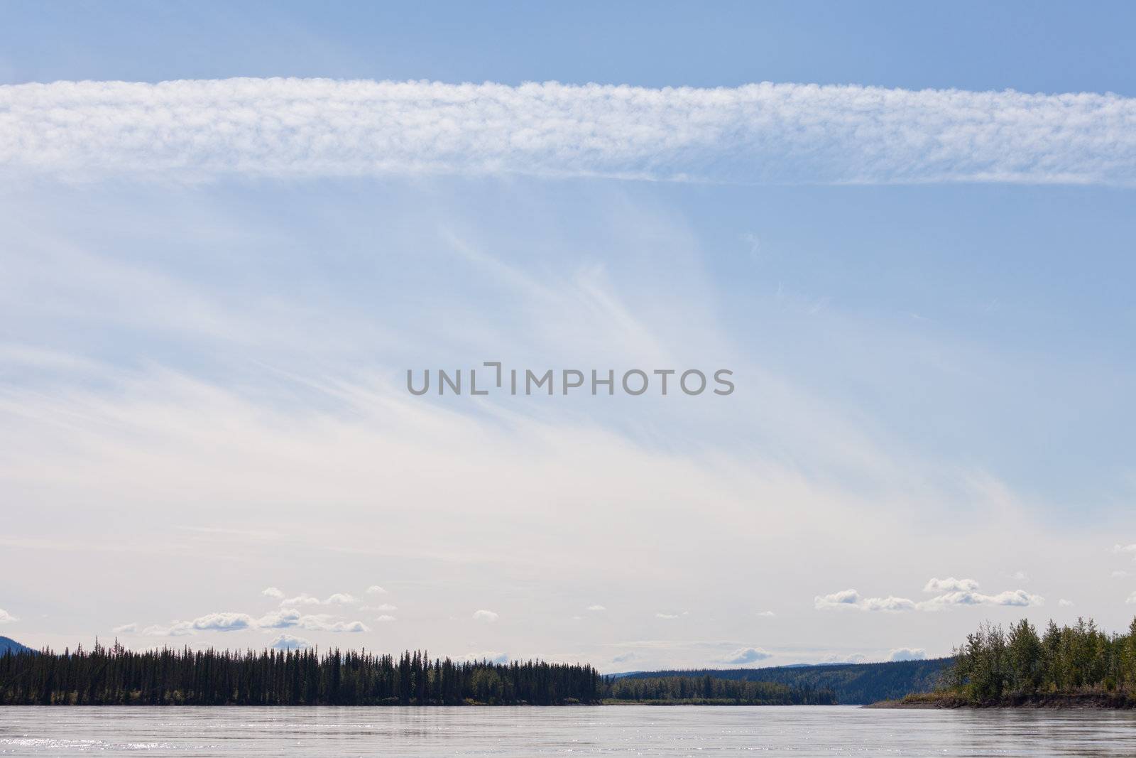 Some summer clouds in blue sky over mighty stream Yukon River, Yukon Territory, Canada, near Dawson City forming a beautiful northern riverscape.