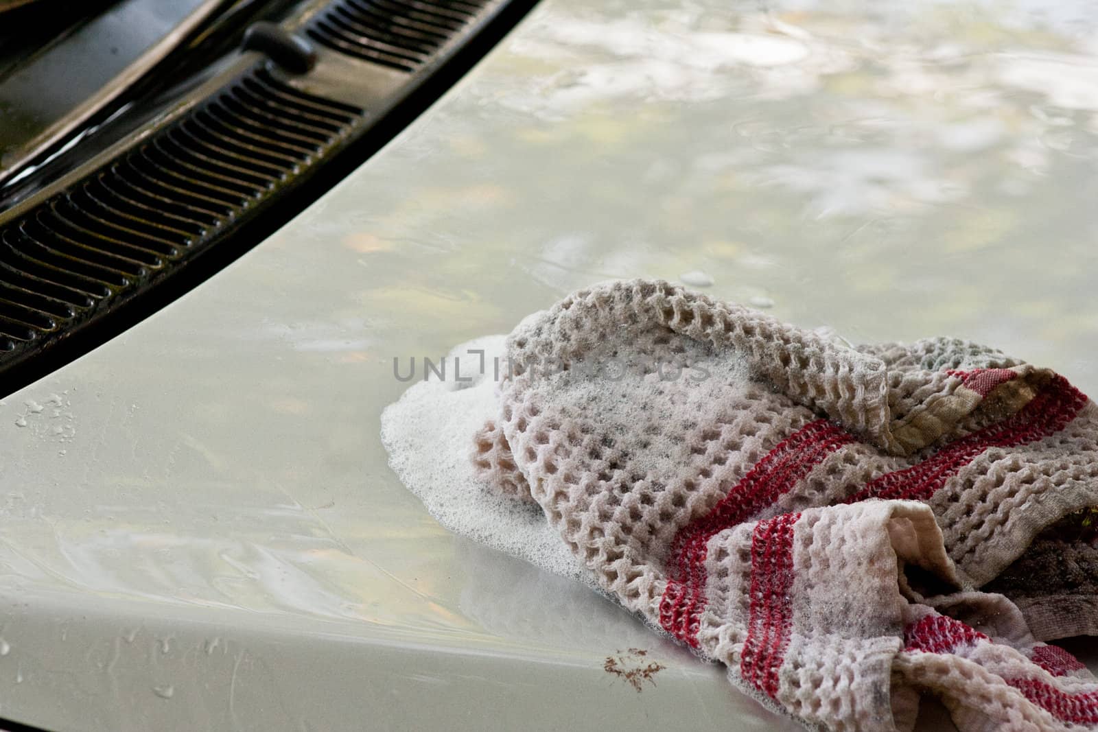 Washing the hood of a car with a cloth and soapy water.