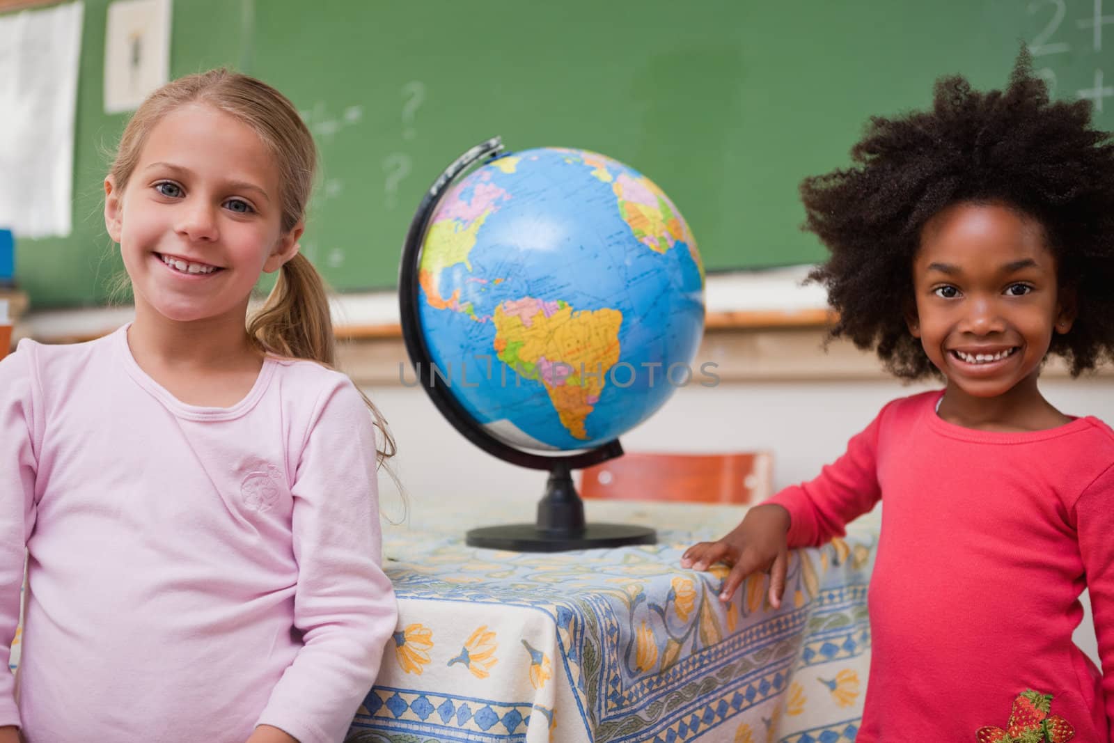 Cute schoolgirls posing with a globe in a classroom
