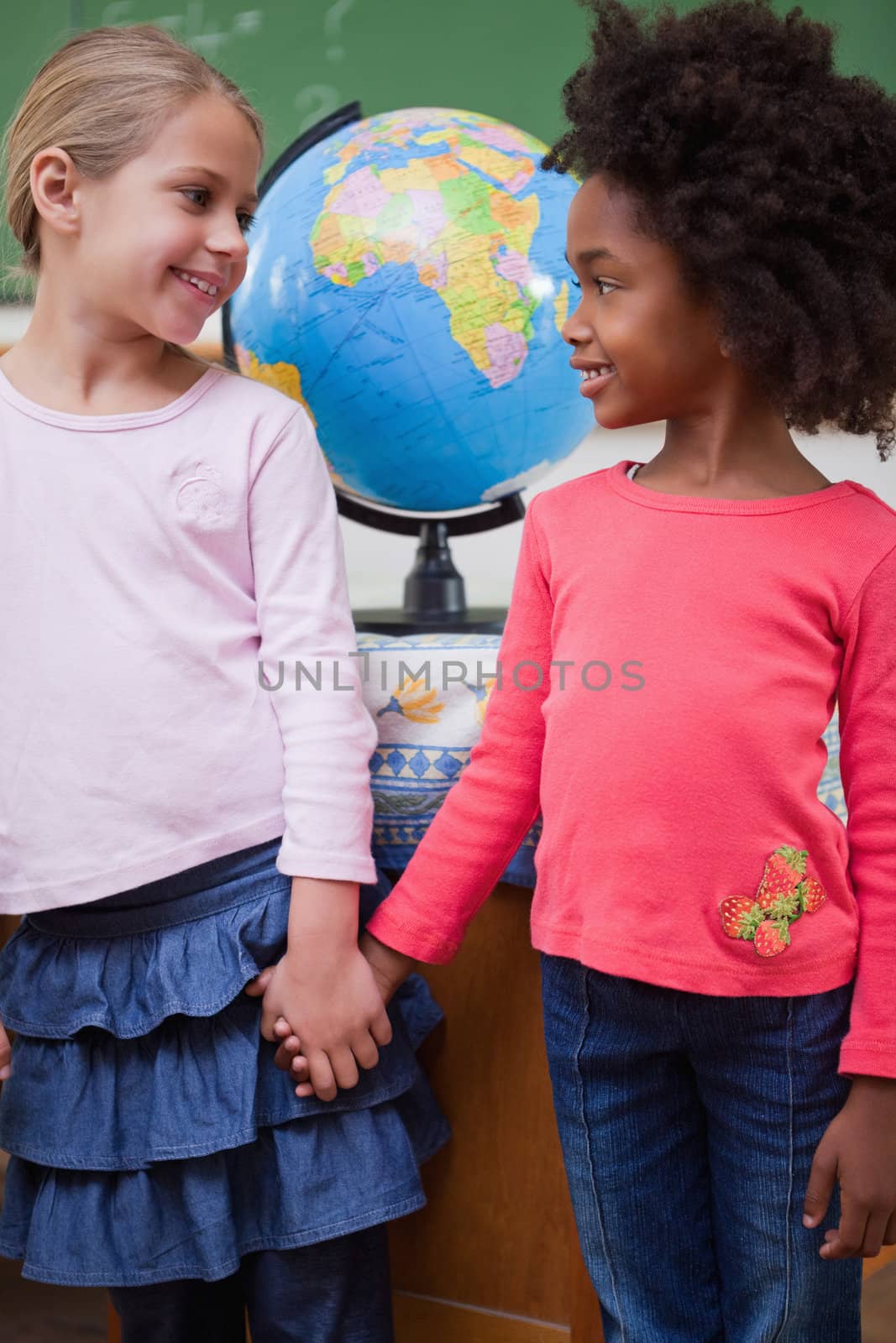 Portrait of smiling schoolgirls holding hands in a classroom