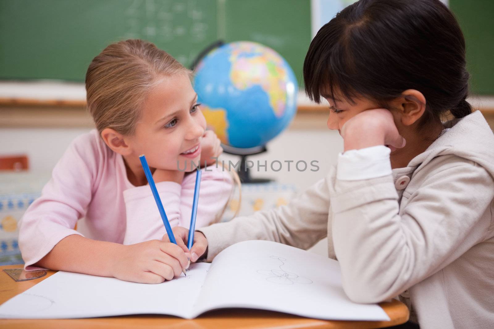 Cute schoolgirls doing classwork while looking at each other
