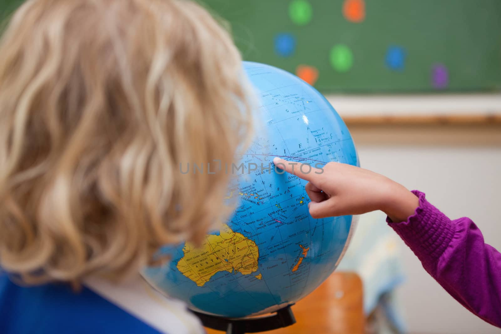 Finger of a little girl showing a country to a classmate on a globe