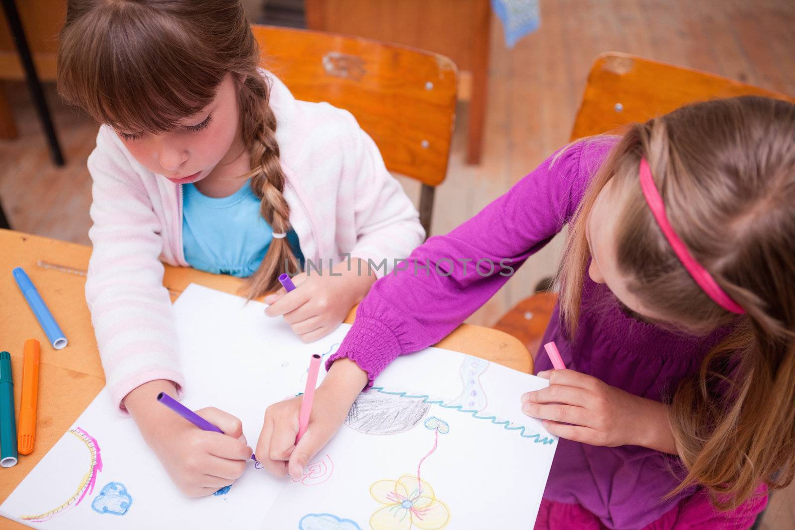 Schoolgirls drawing in a coloring book in a classroom
