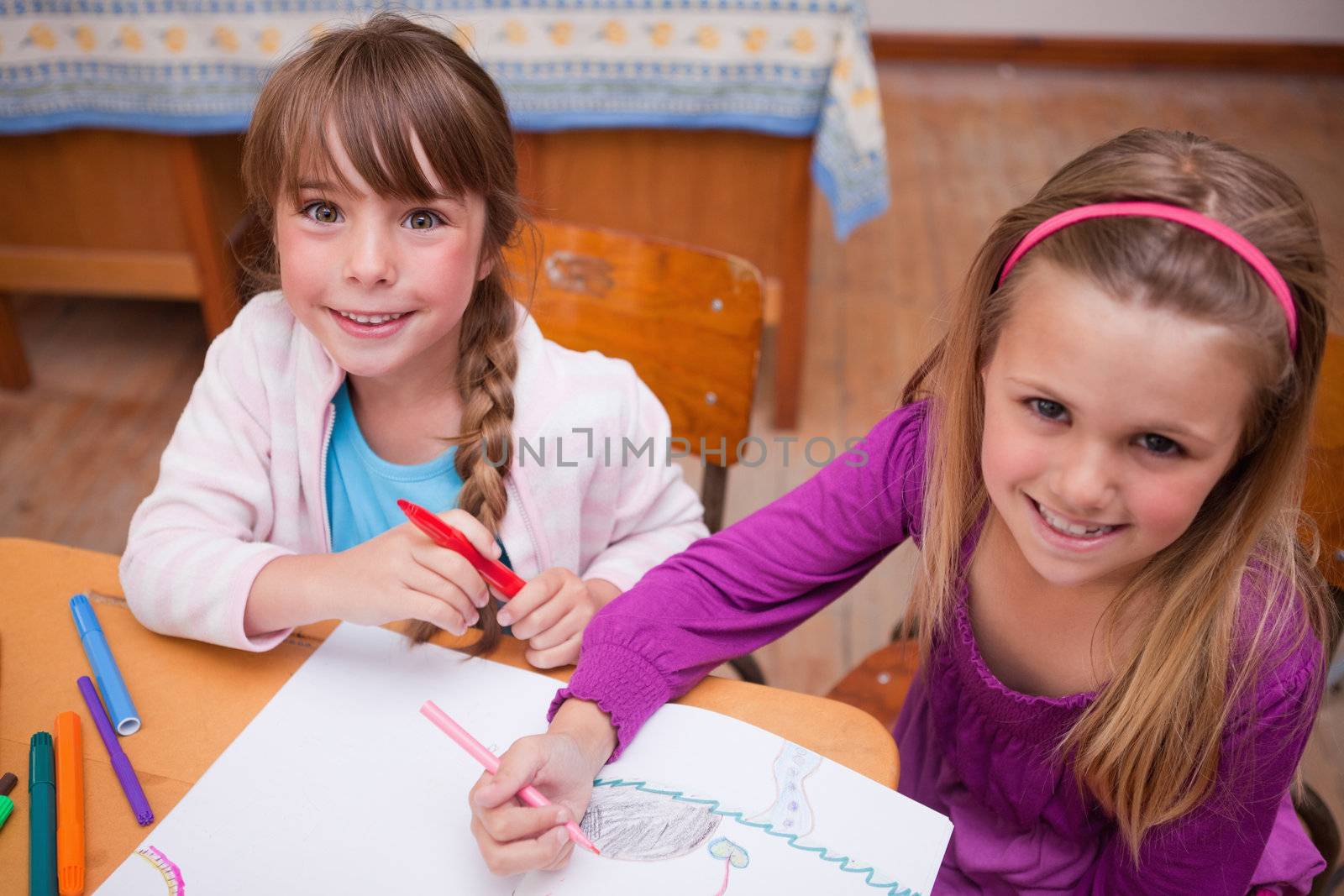 Cute schoolgirls drawing in a coloring book in a classroom