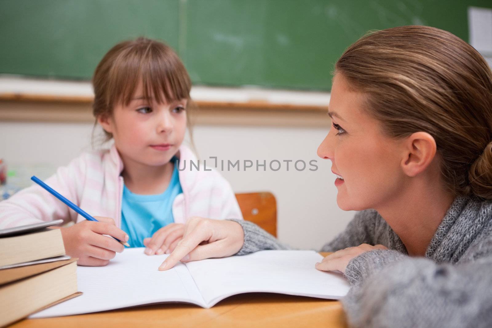 Schoolgirl writing a while her teacher is talking in a classroom
