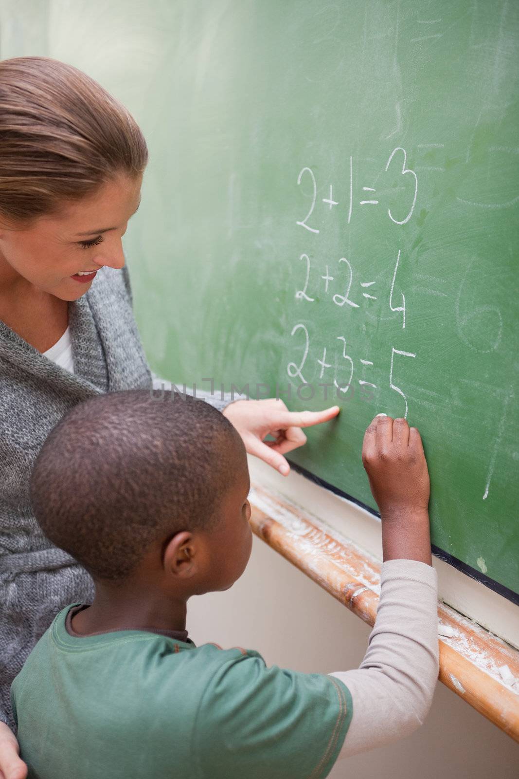 Portrait of a cute teacher and a pupil making an addition on a blackboard
