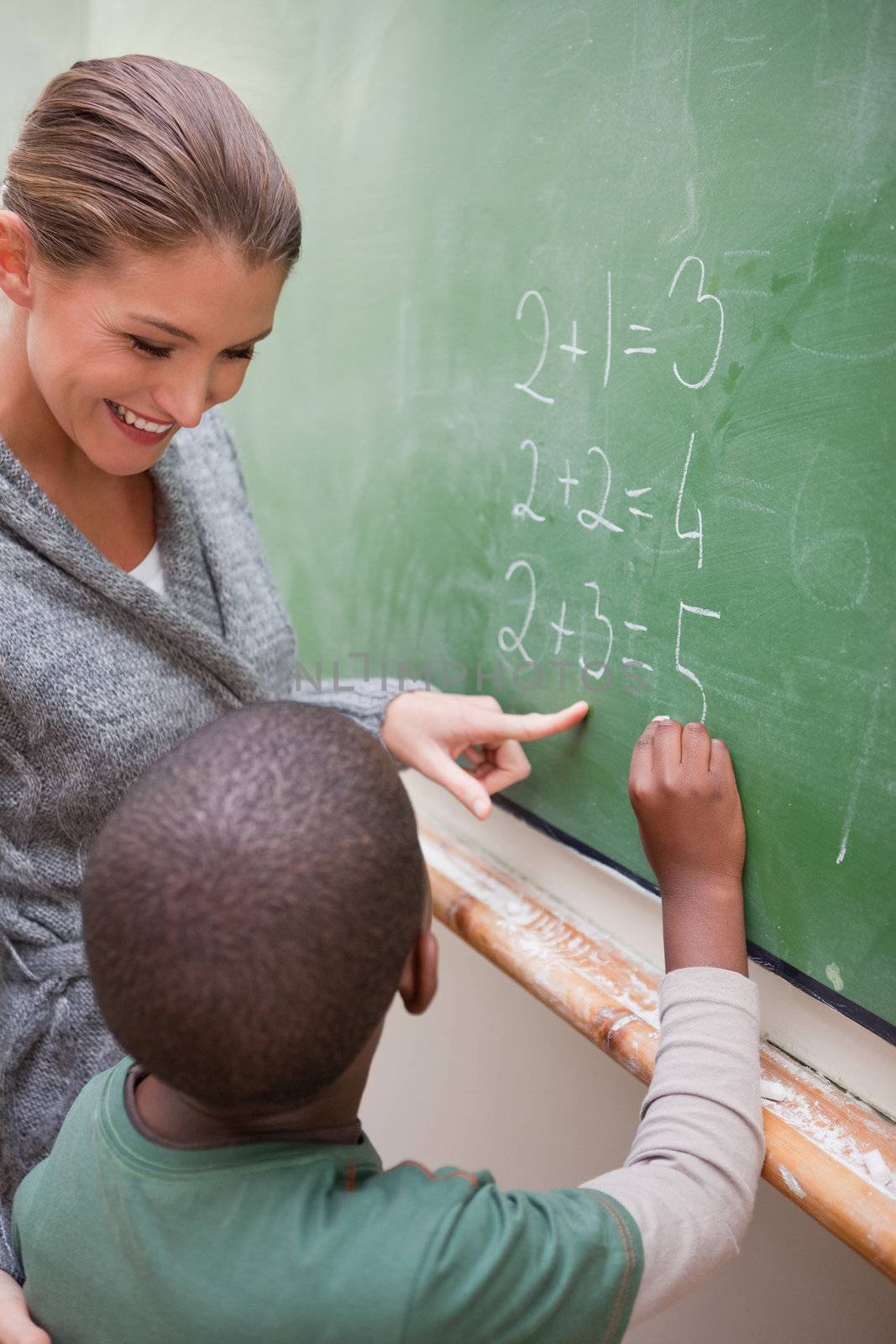 Portrait of a beautiful teacher and a pupil making an addition on a blackboard