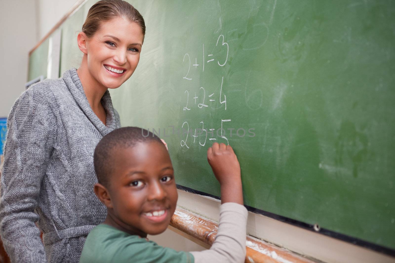 Smiling teacher and a pupil making an addition on a blackboard