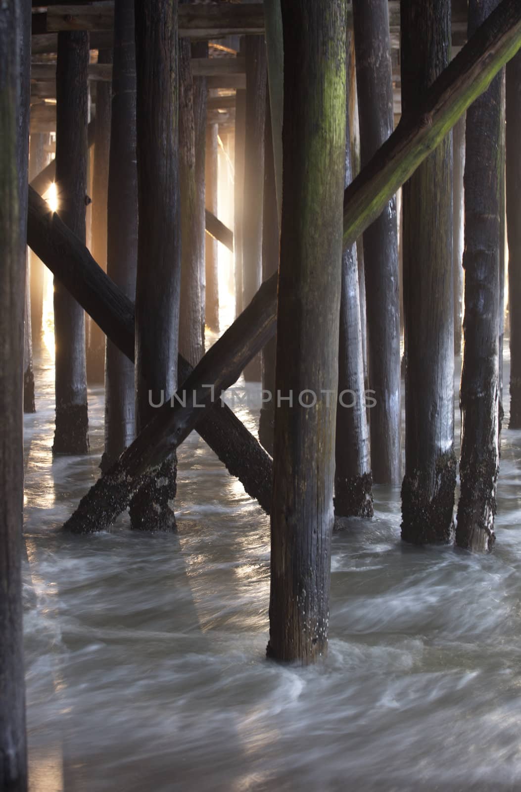 Wooden pilings beneath the pier with flowing tides and morning light visible; location is New Jersey shore, Seaside Heights, Casino Pier.  Motion blur, slow shutter speed used. 