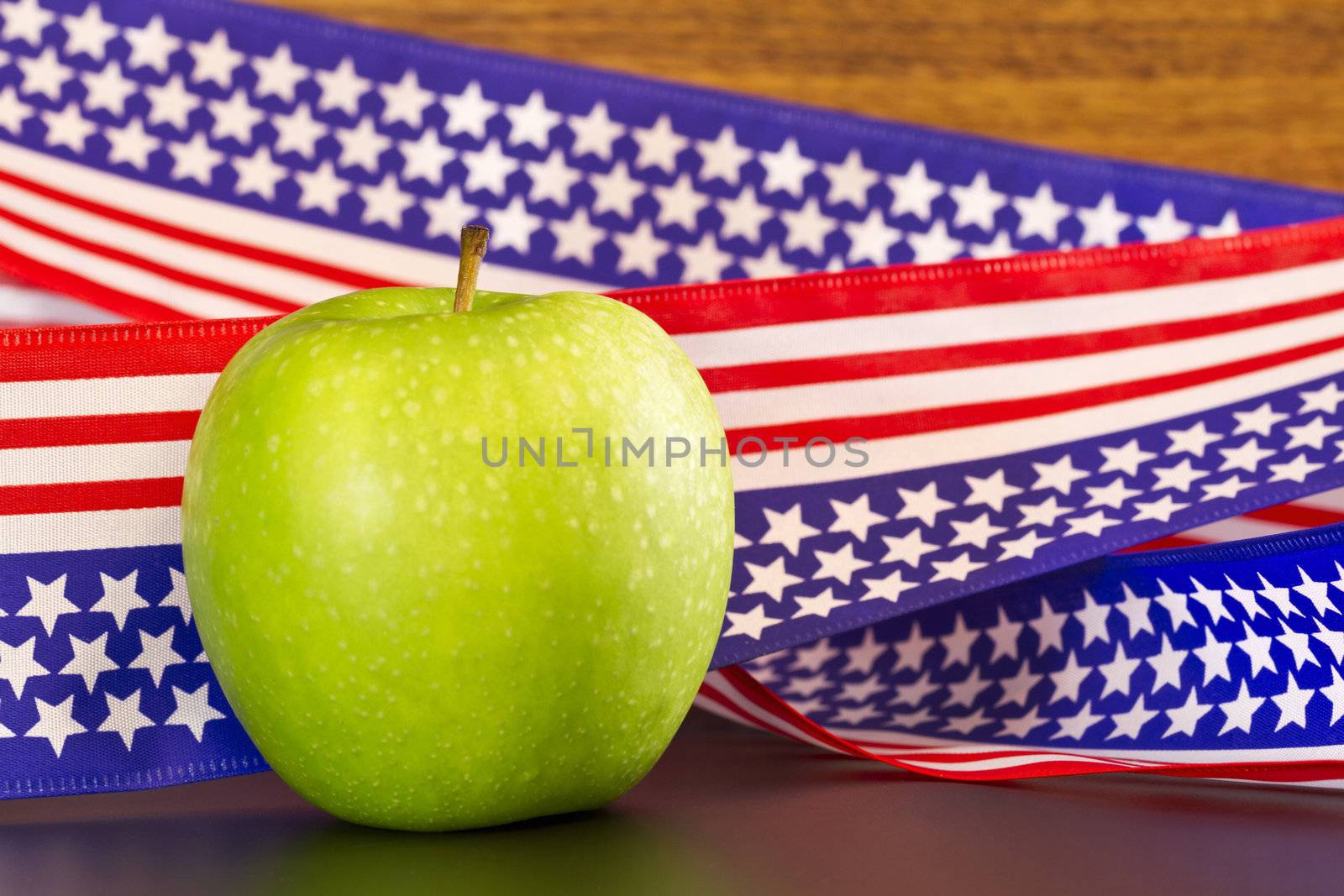 Green apple placed on  stars and stripes ribbon with USA flag motif; apple suggests school, education, environment, as well as health, food, obesity, fitness issues that impact the nation. 