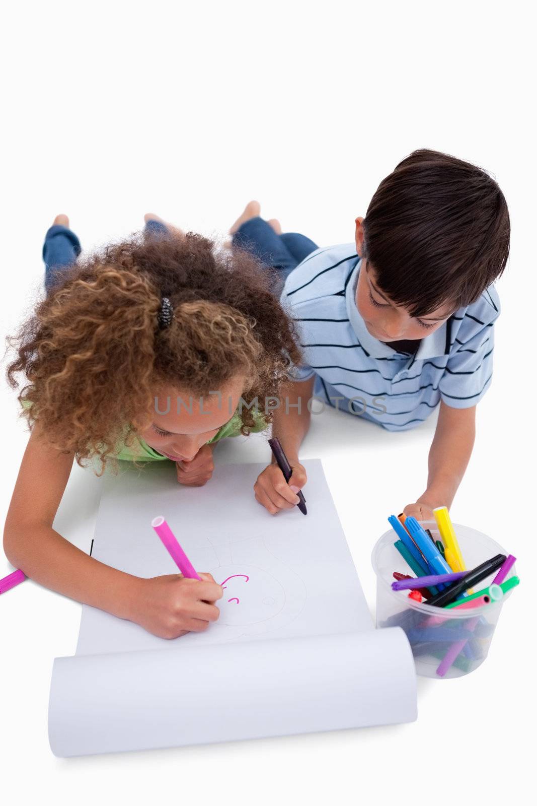 Portrait of children drawing while lying on the floor against a white background