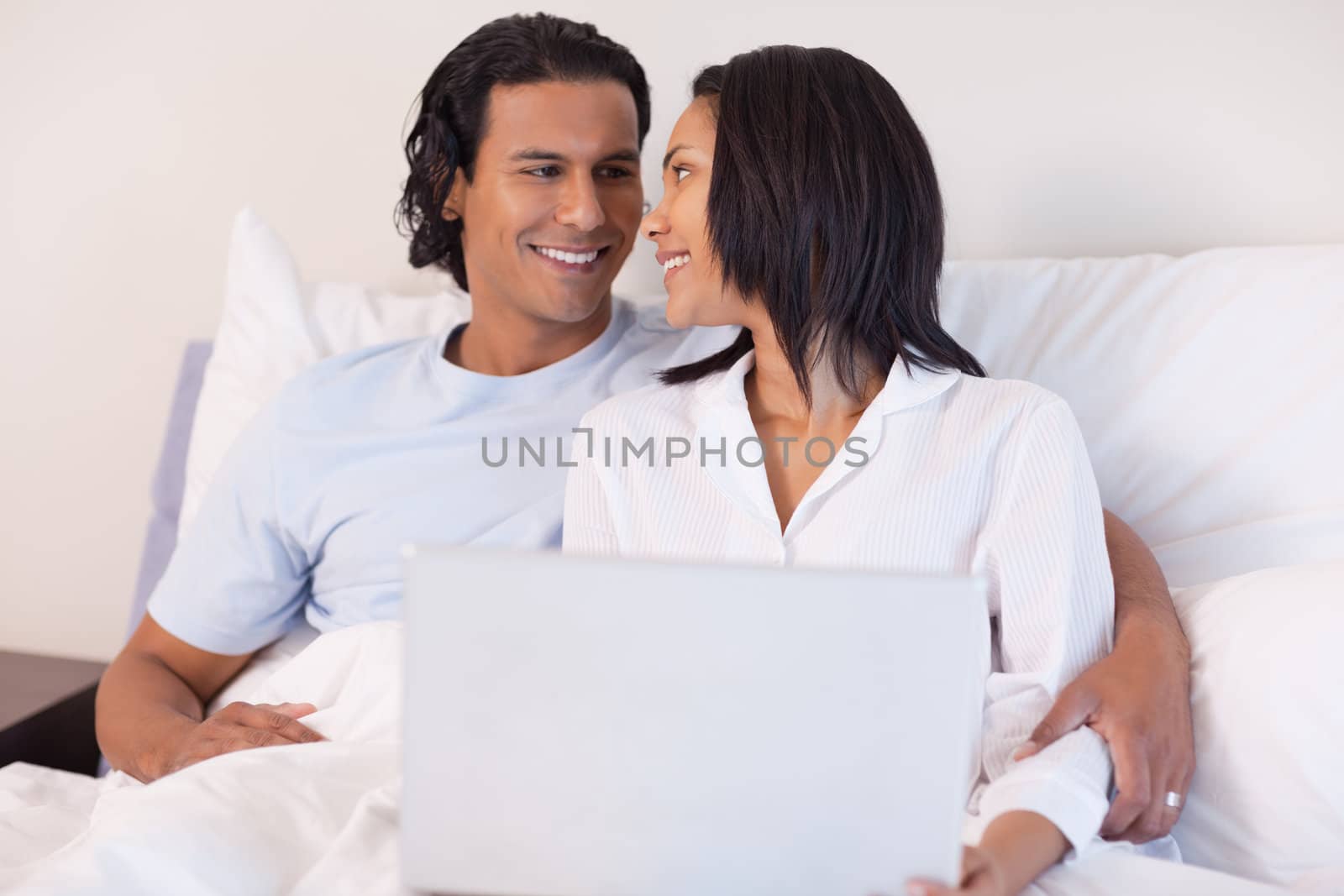 Smiling young couple sitting on the bed with their laptop