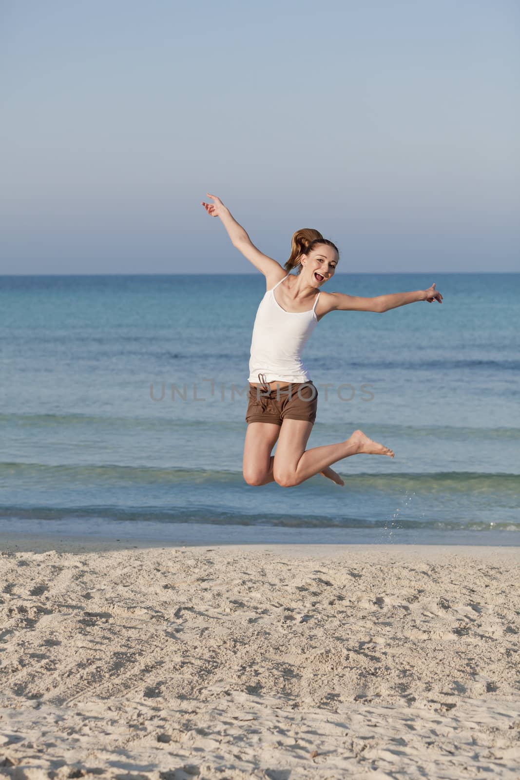 Girl young cheerful woman jumping in the air on the beach in the sand in the morning on the sea in summer vacation