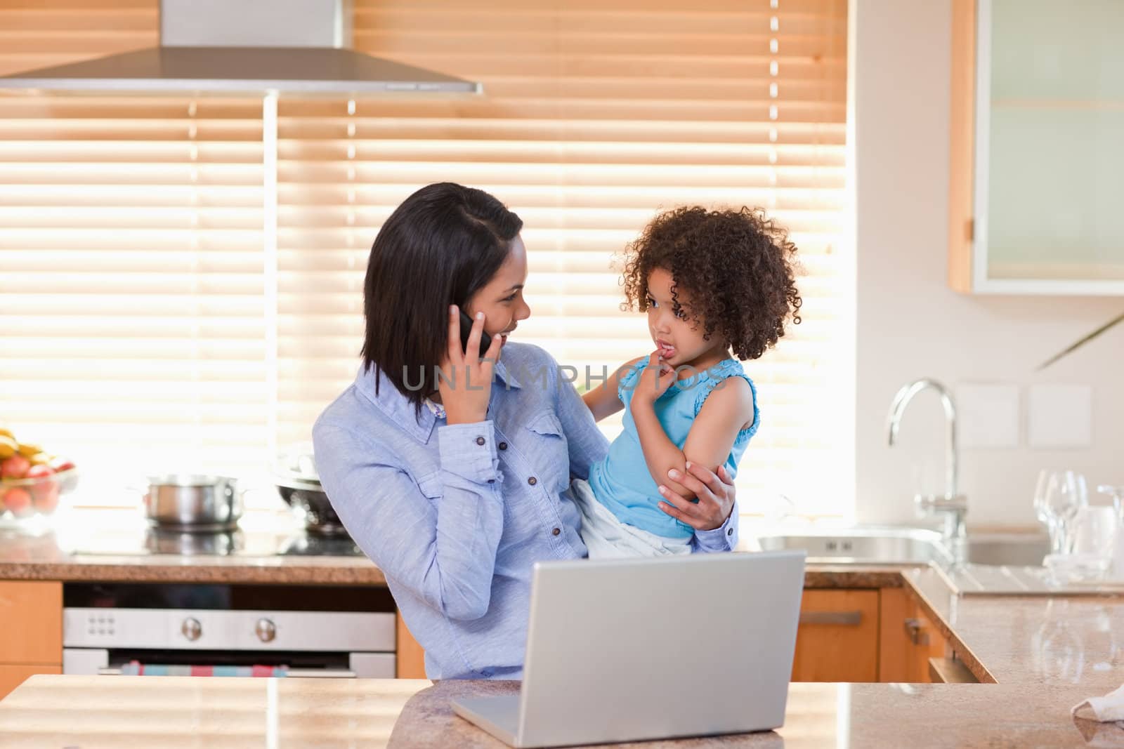 Young mother and daughter with cellphone and notebook in the kitchen together