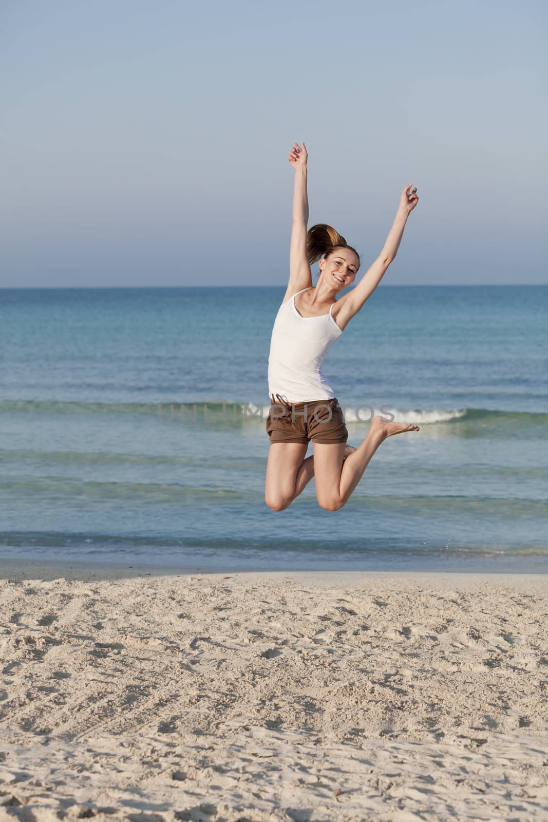 Girl young cheerful woman jumping in the air on the beach in the sand in the morning on the sea in summer vacation