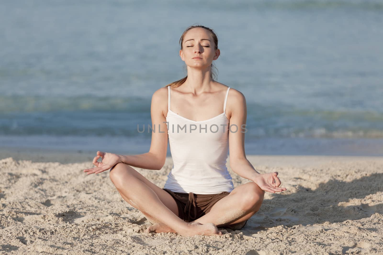 Young sporty woman doing sport yoga on the beach in the sand on the beach in the sun