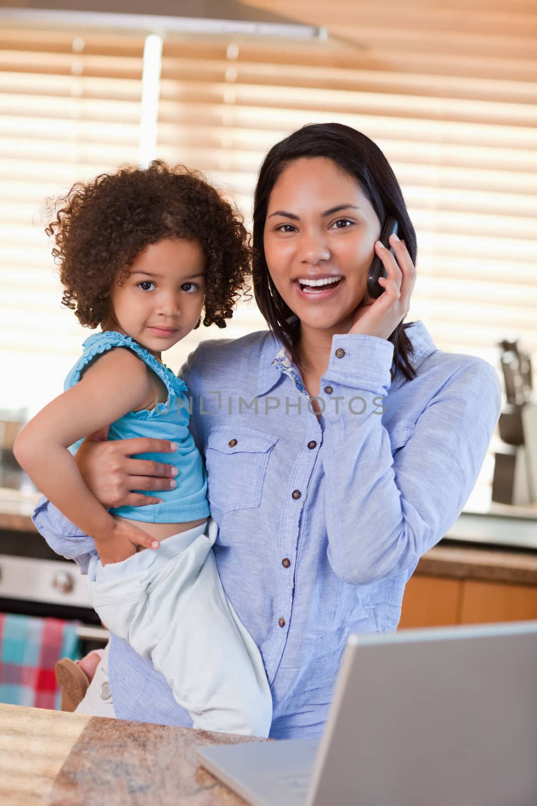 Young mother and daughter using cellphone in the kitchen together