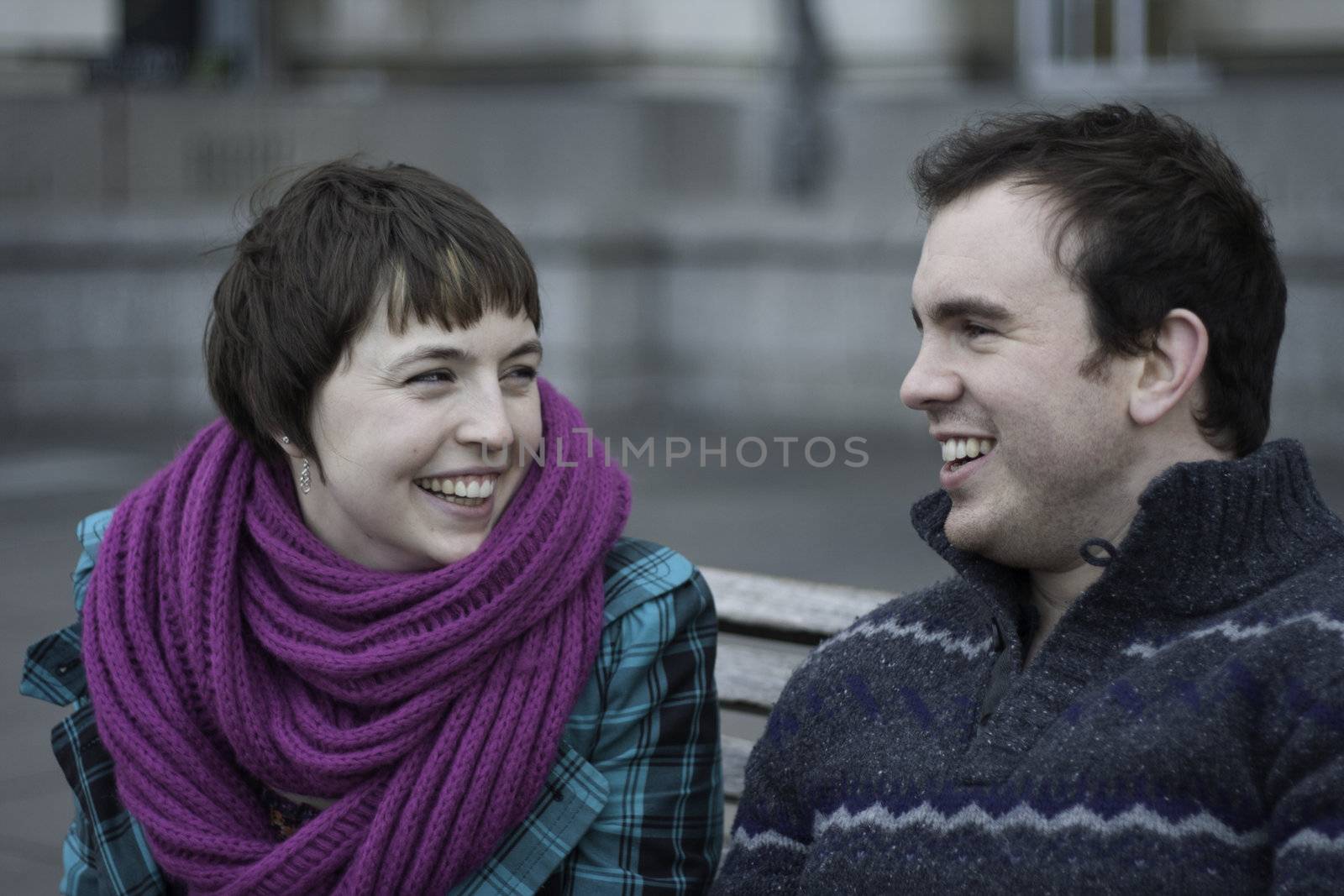 Laughing young couple seated on a park bench on a grey winter day enjoying the cold weather
