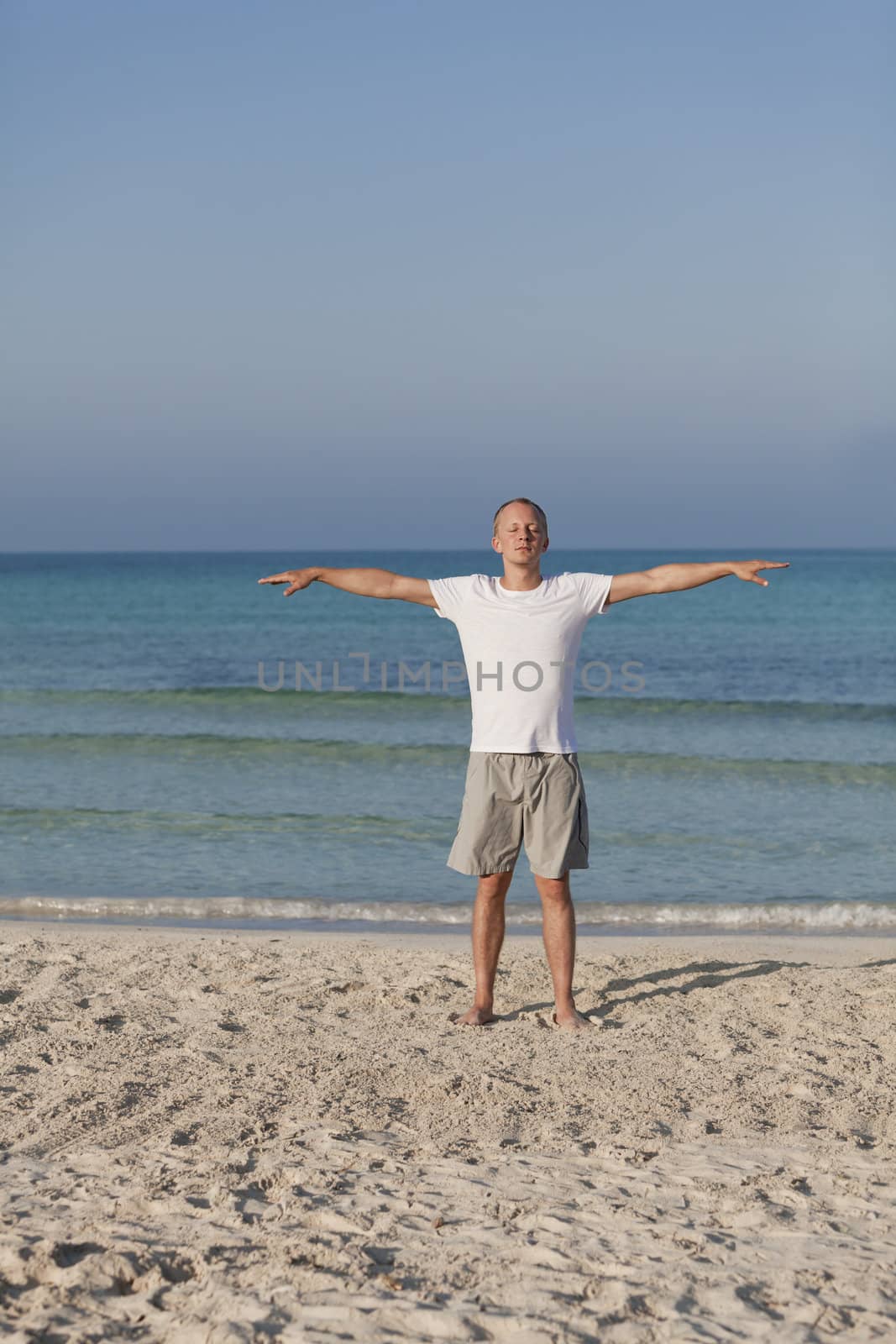 Young athletic man doing sport yoga on the beach in the sand on the beach in the sun