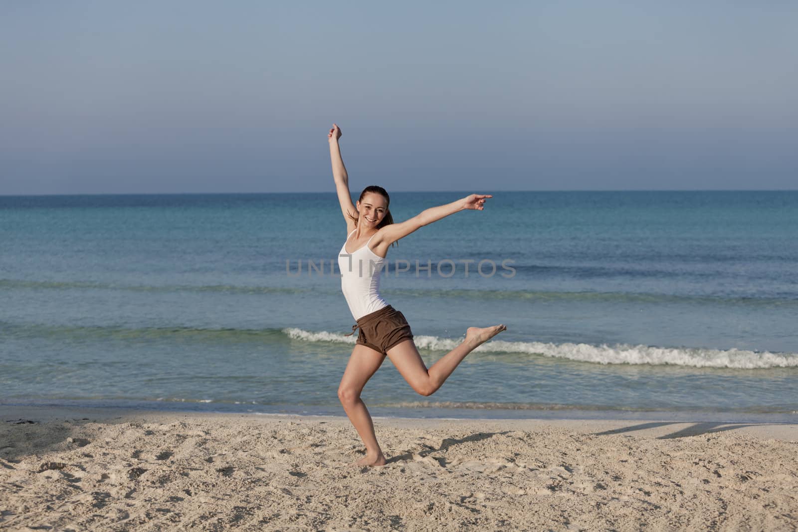 Girl young cheerful woman jumping in the air on the beach in the sand in the morning on the sea in summer vacation