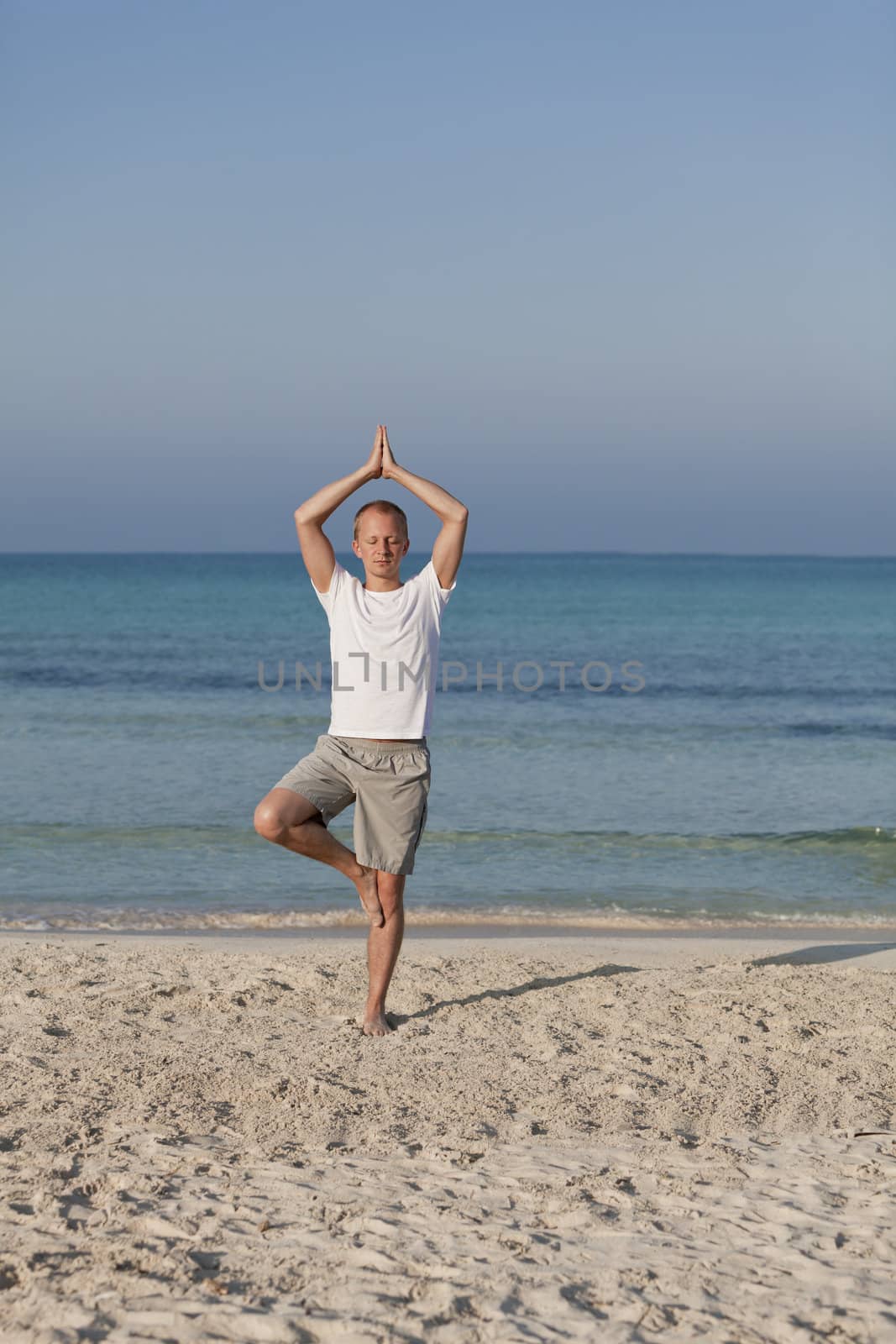 Young athletic man doing sport yoga on the beach in the sand on the beach in the sun