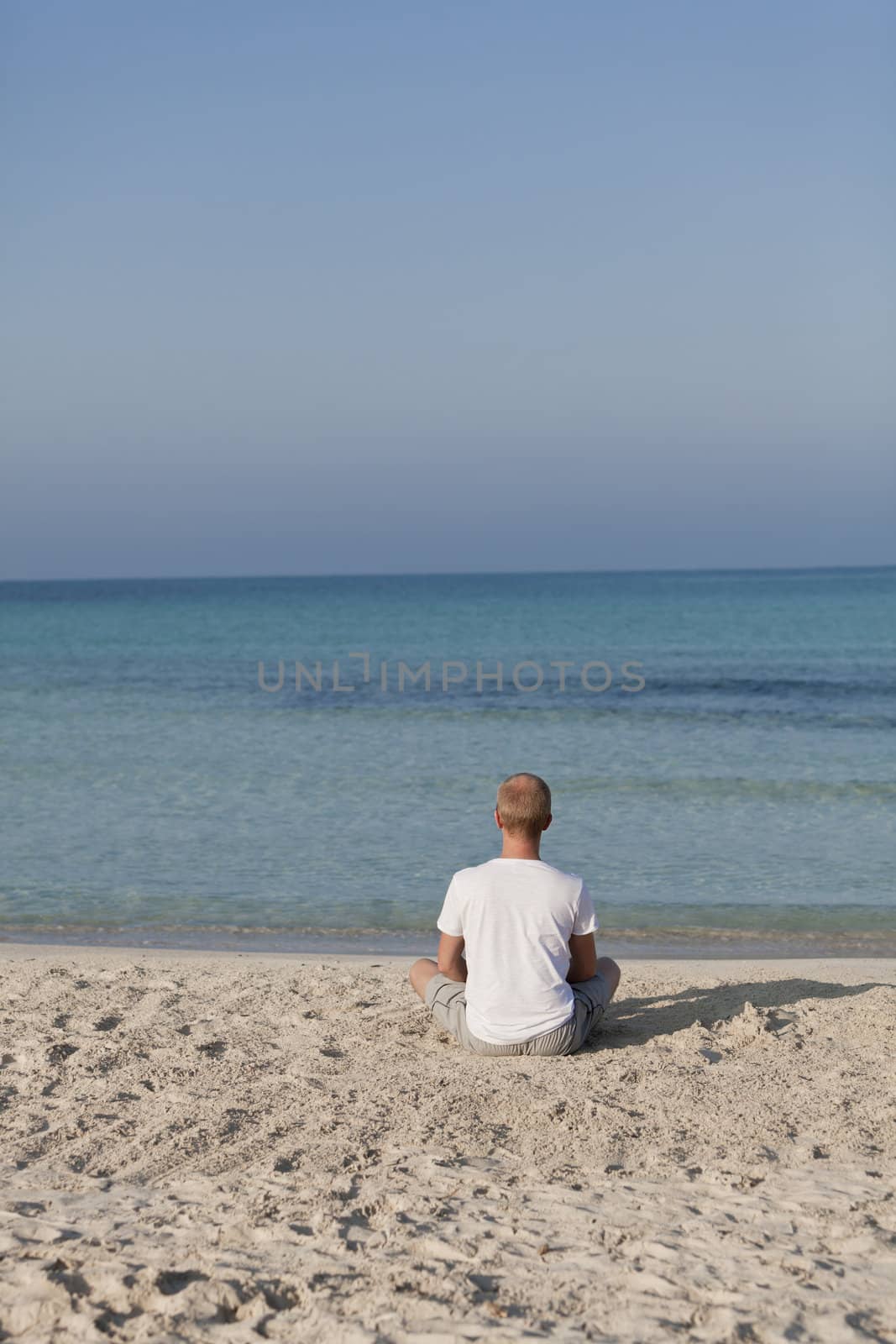 Young athletic man doing sport yoga on the beach in the sand on the beach in the sun