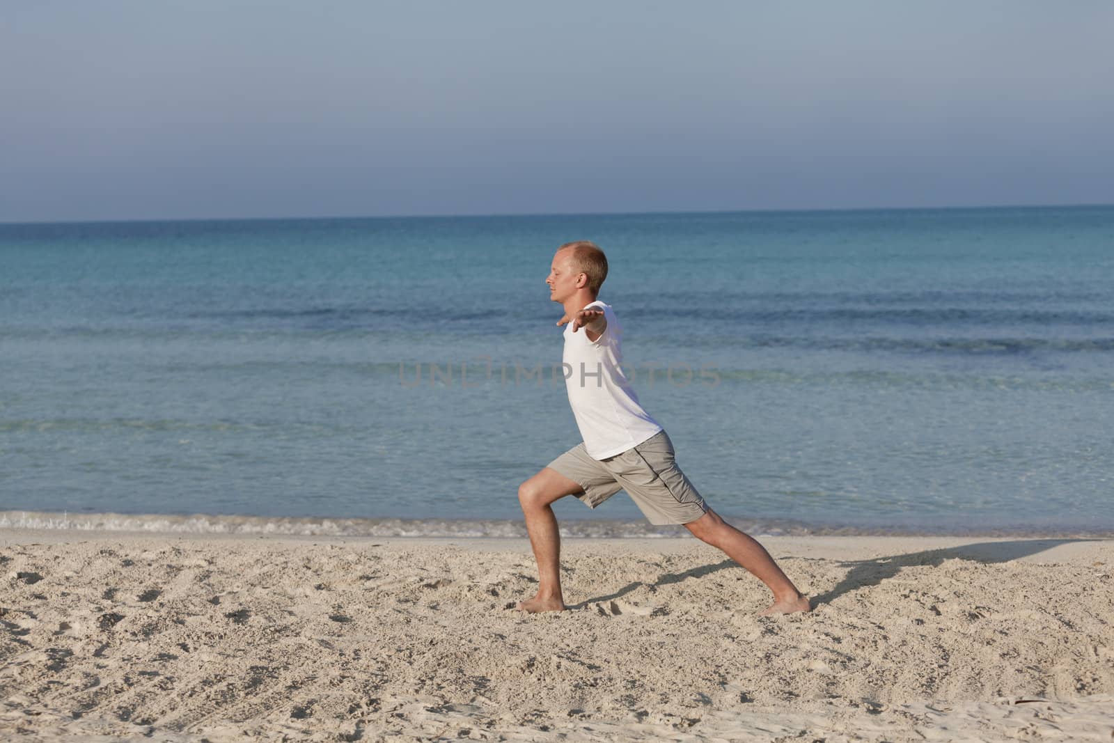 Young athletic man doing sport yoga on the beach in the sand on the beach in the sun