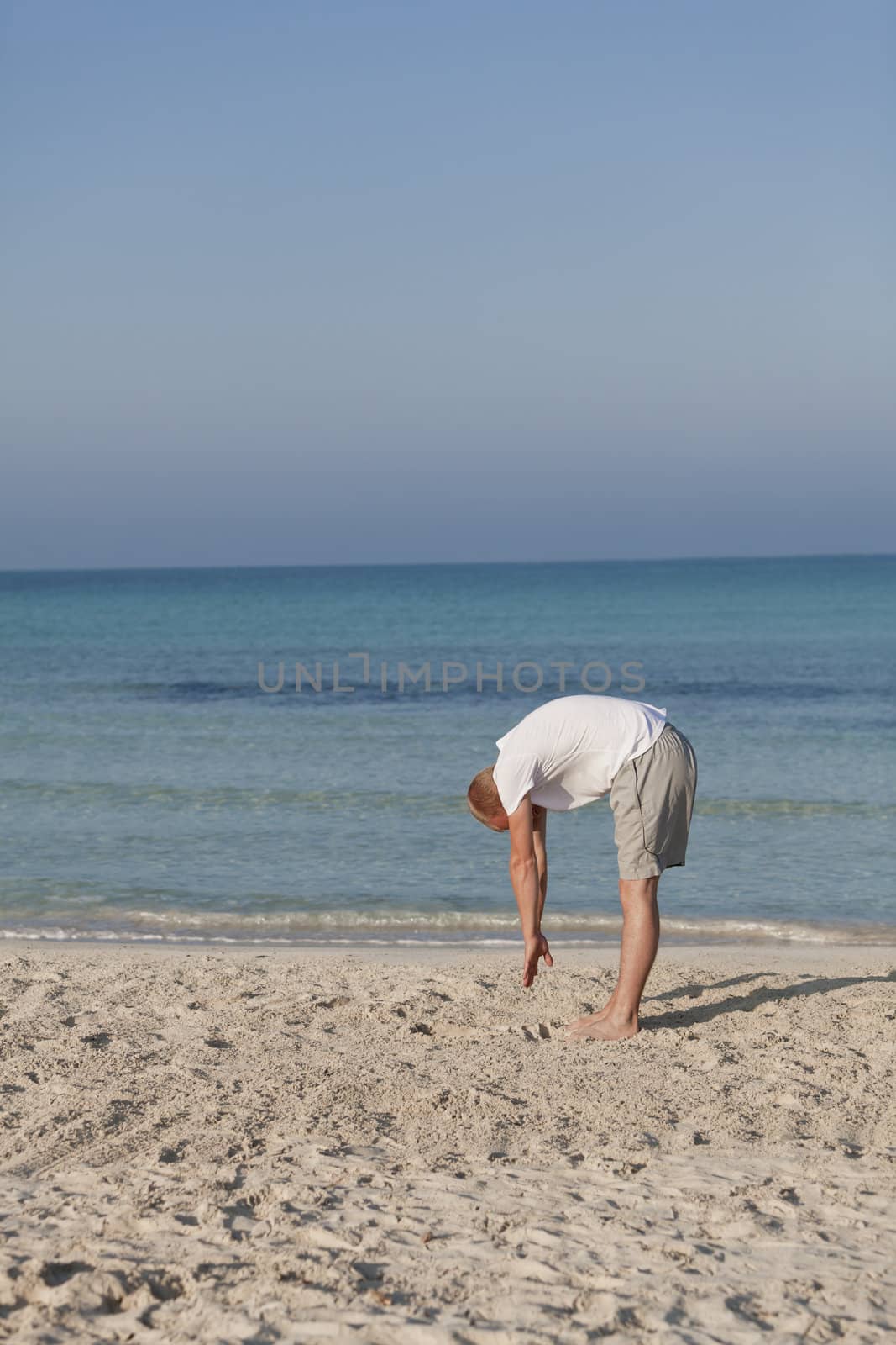 Young athletic man doing sport yoga on the beach in the sand on the beach in the sun