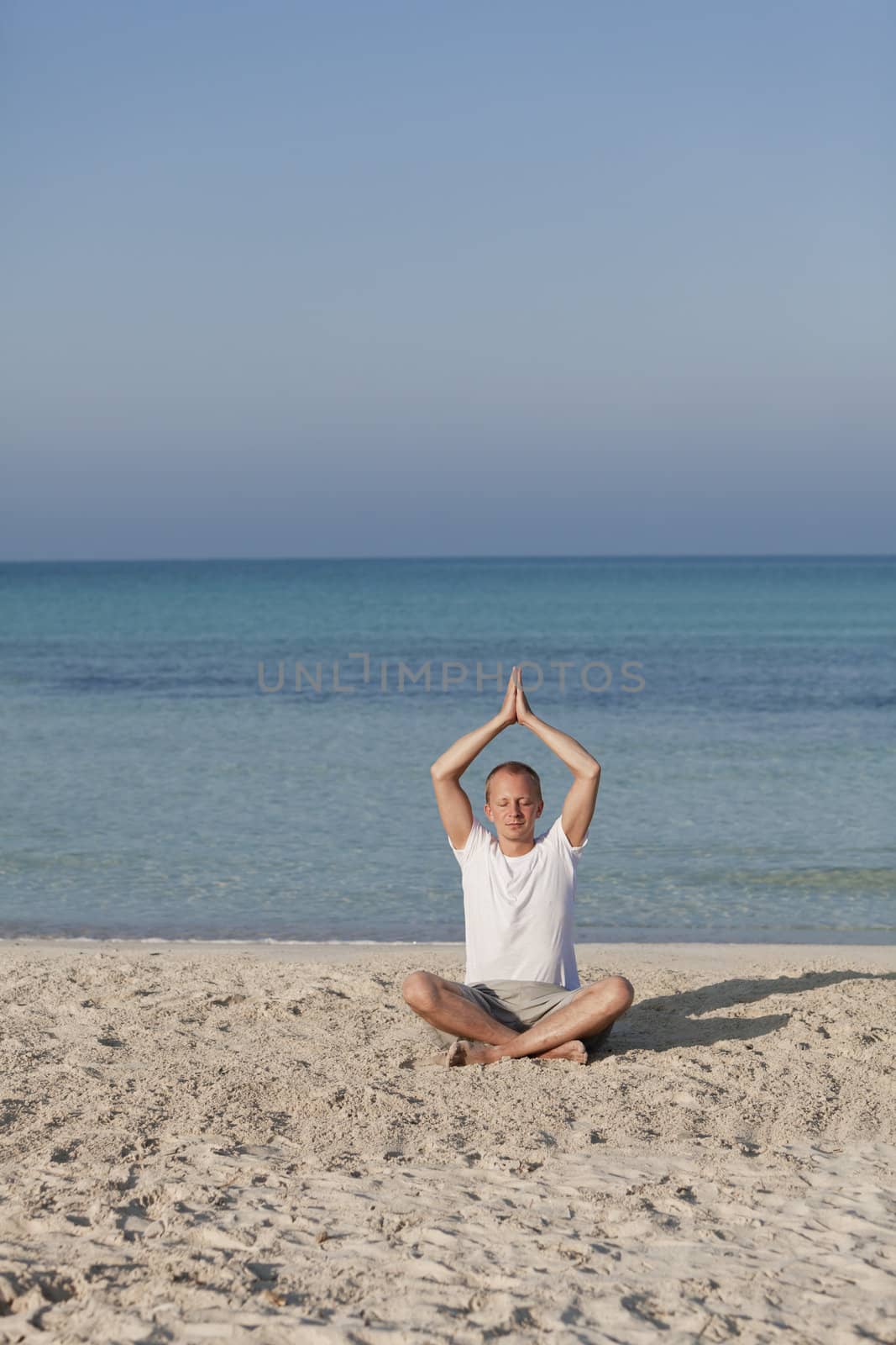 Young athletic man doing sport yoga on the beach in the sand on the beach in the sun