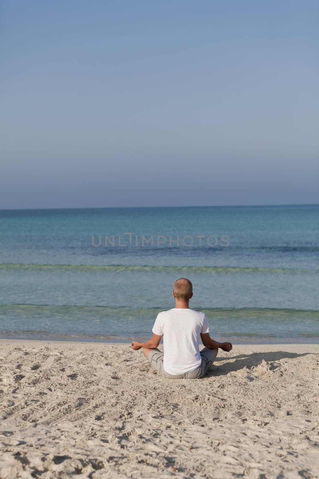 Young athletic man doing sport yoga on the beach in the sand on the beach in the sun