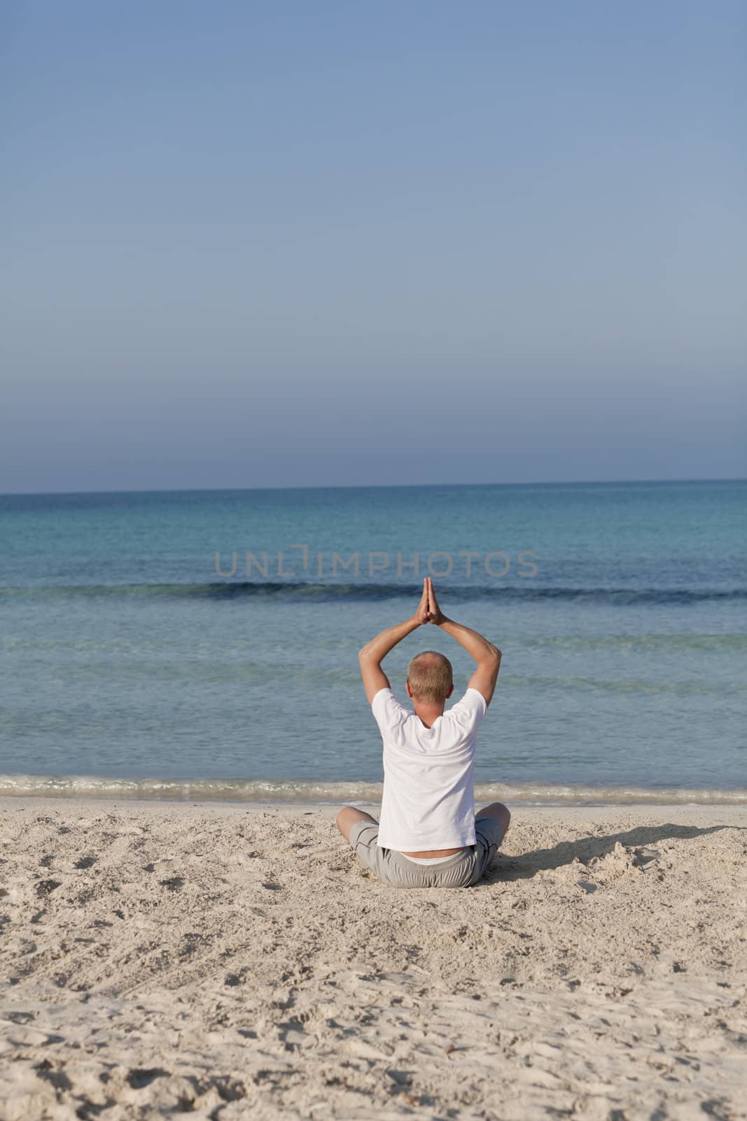 Young athletic man doing sport yoga on the beach in the sand on the beach in the sun