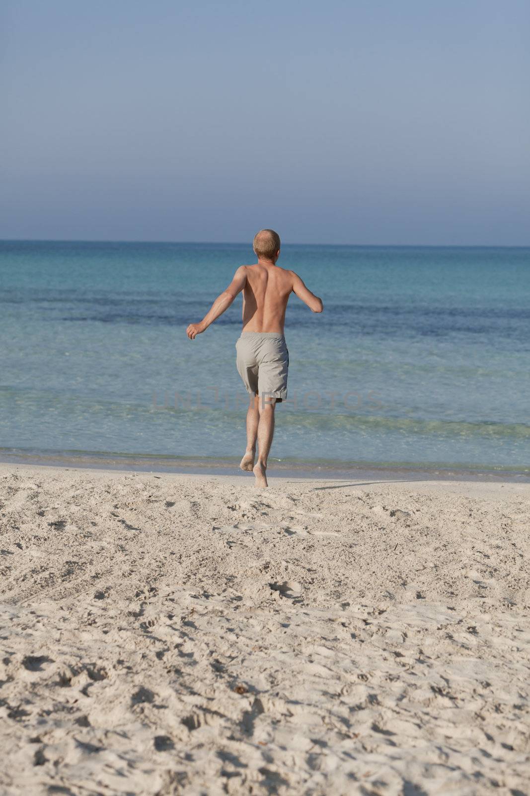 Young man running on the beach young running in water with splashes and fun in the summer holidays