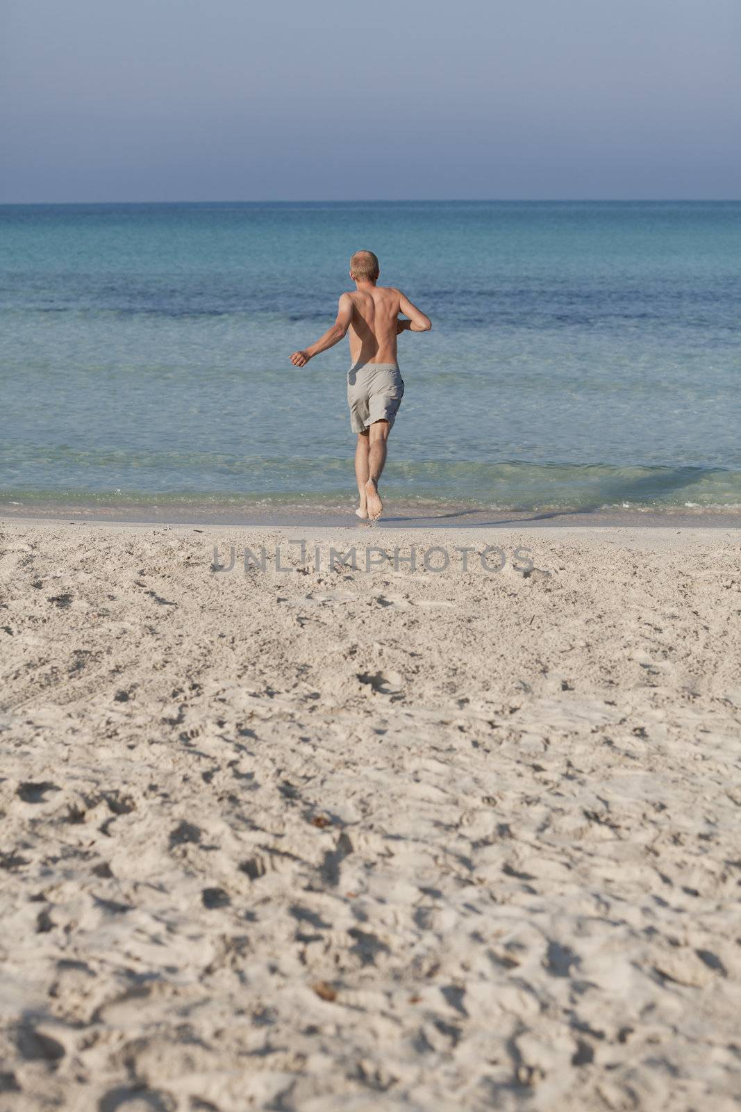 Young man running on the beach young running in water with splashes and fun in the summer holidays
