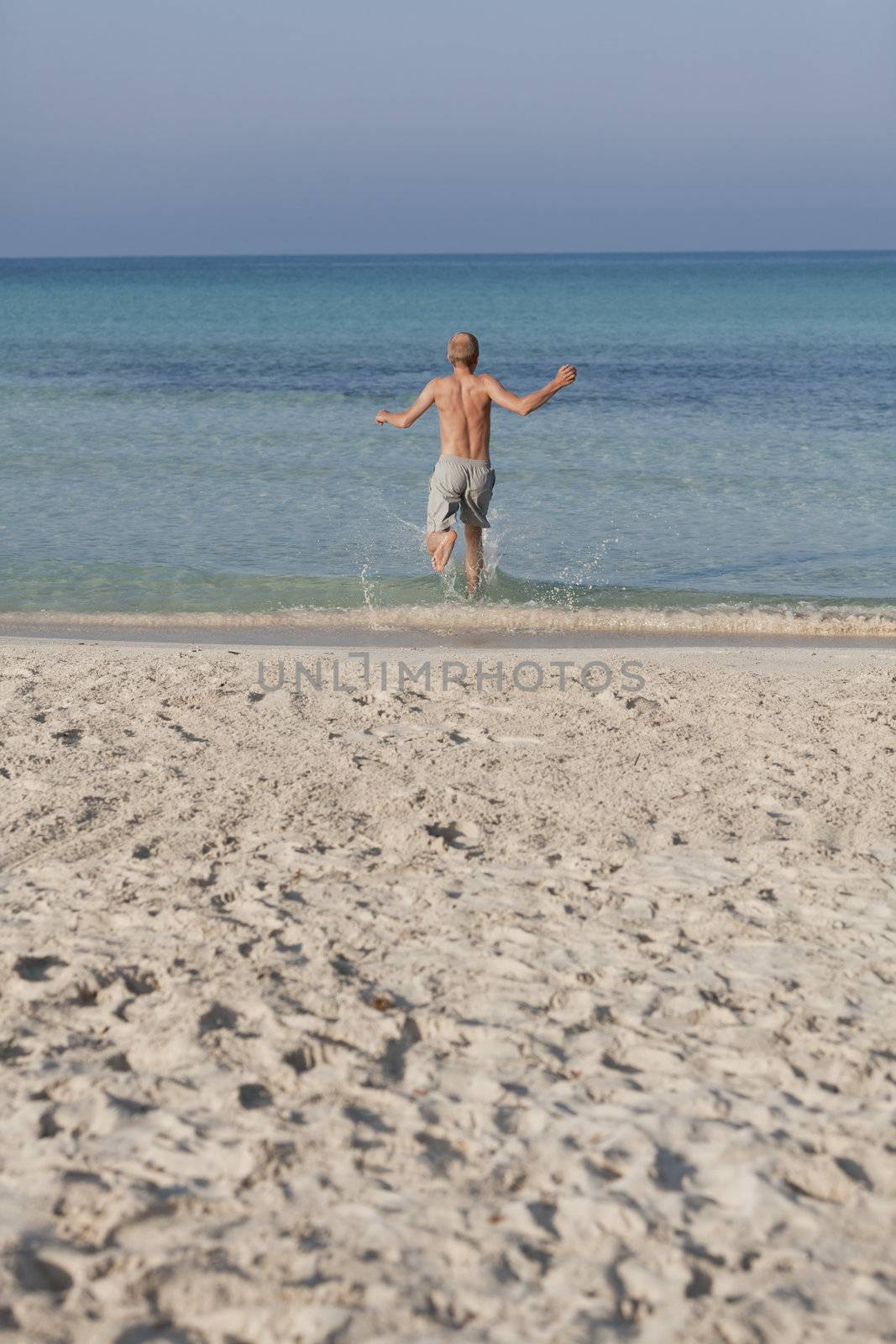 Young man running on the beach young running in water with splashes and fun in the summer holidays