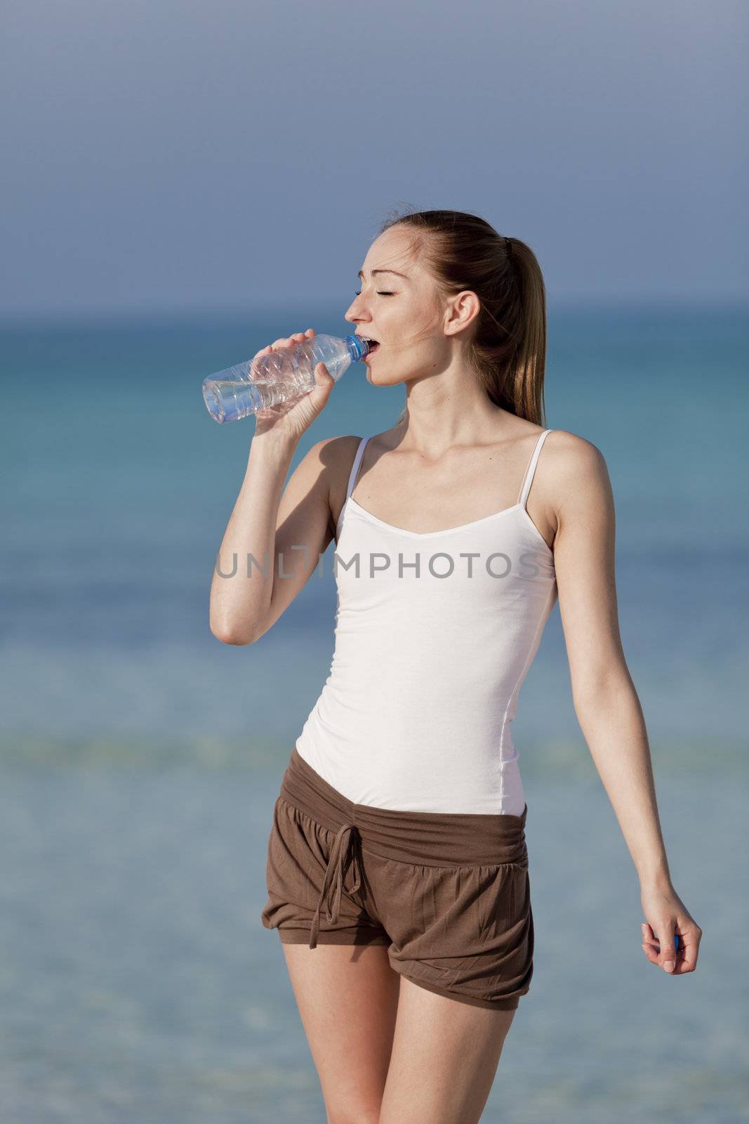 Girl young woman refreshing drinks water from a bottle on the beach by the sea in summer vacation