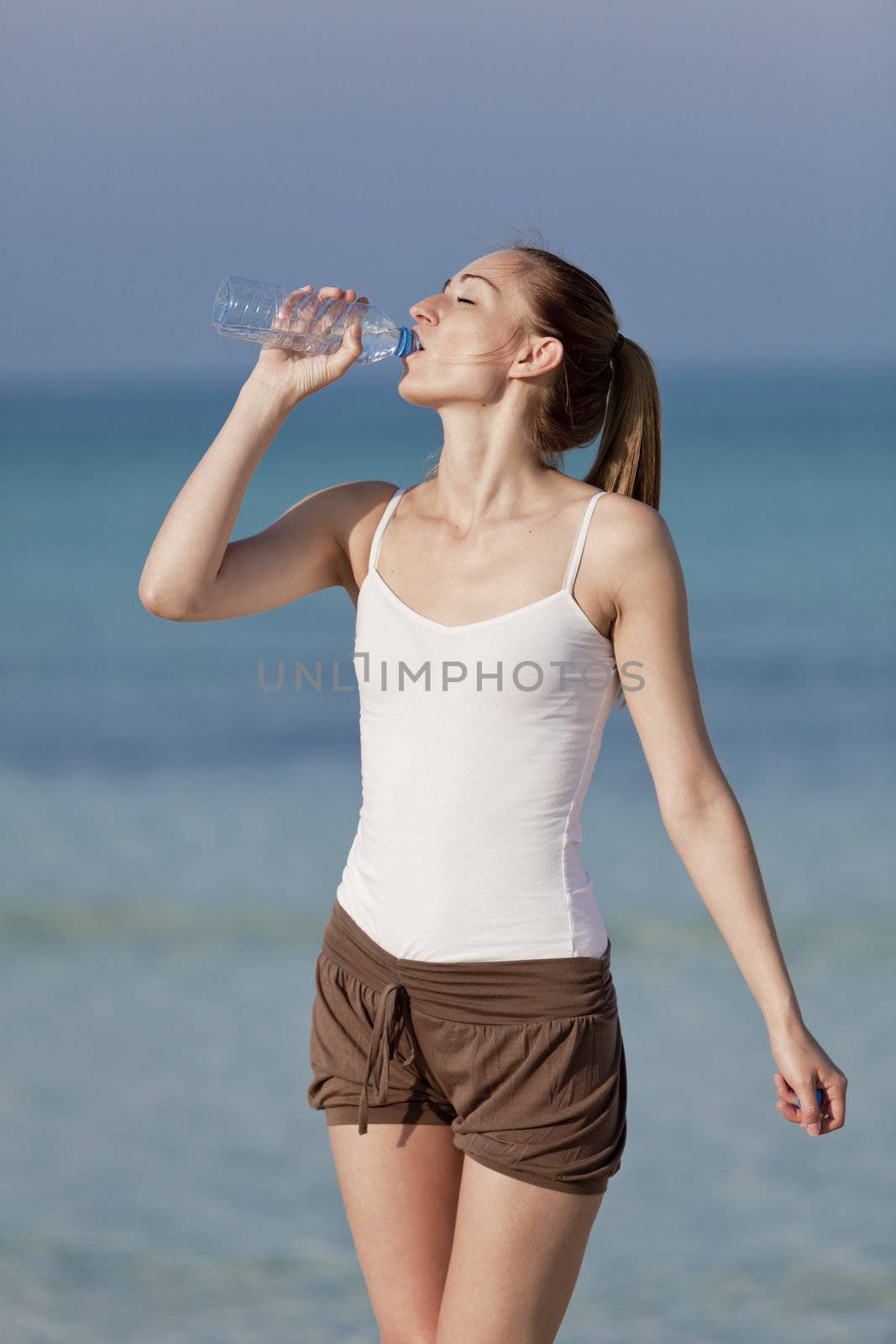 Girl young woman refreshing drinks water from a bottle on the beach by the sea in summer vacation