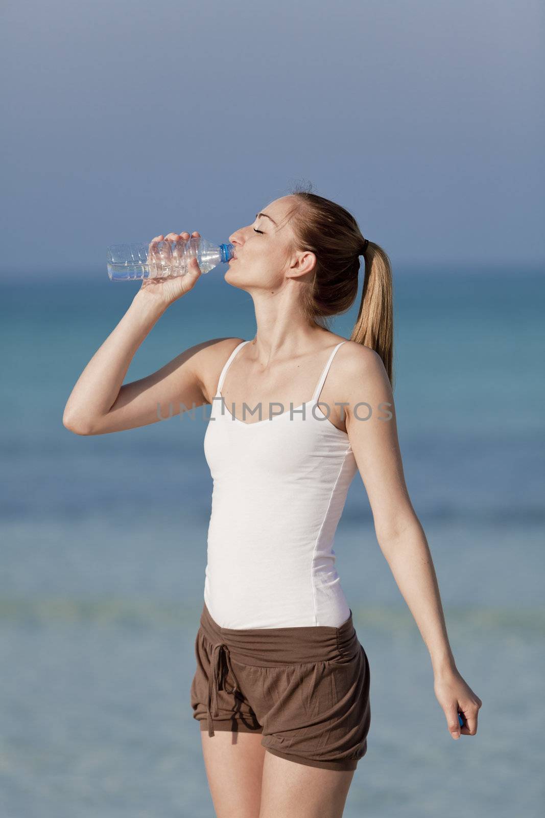 Girl young woman refreshing drinks water from a bottle on the beach by the sea in summer vacation