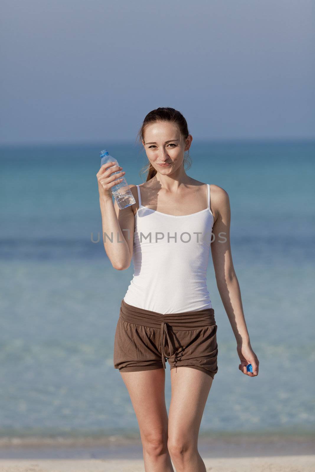 Girl young woman refreshing drinks water from a bottle on the beach by the sea in summer vacation