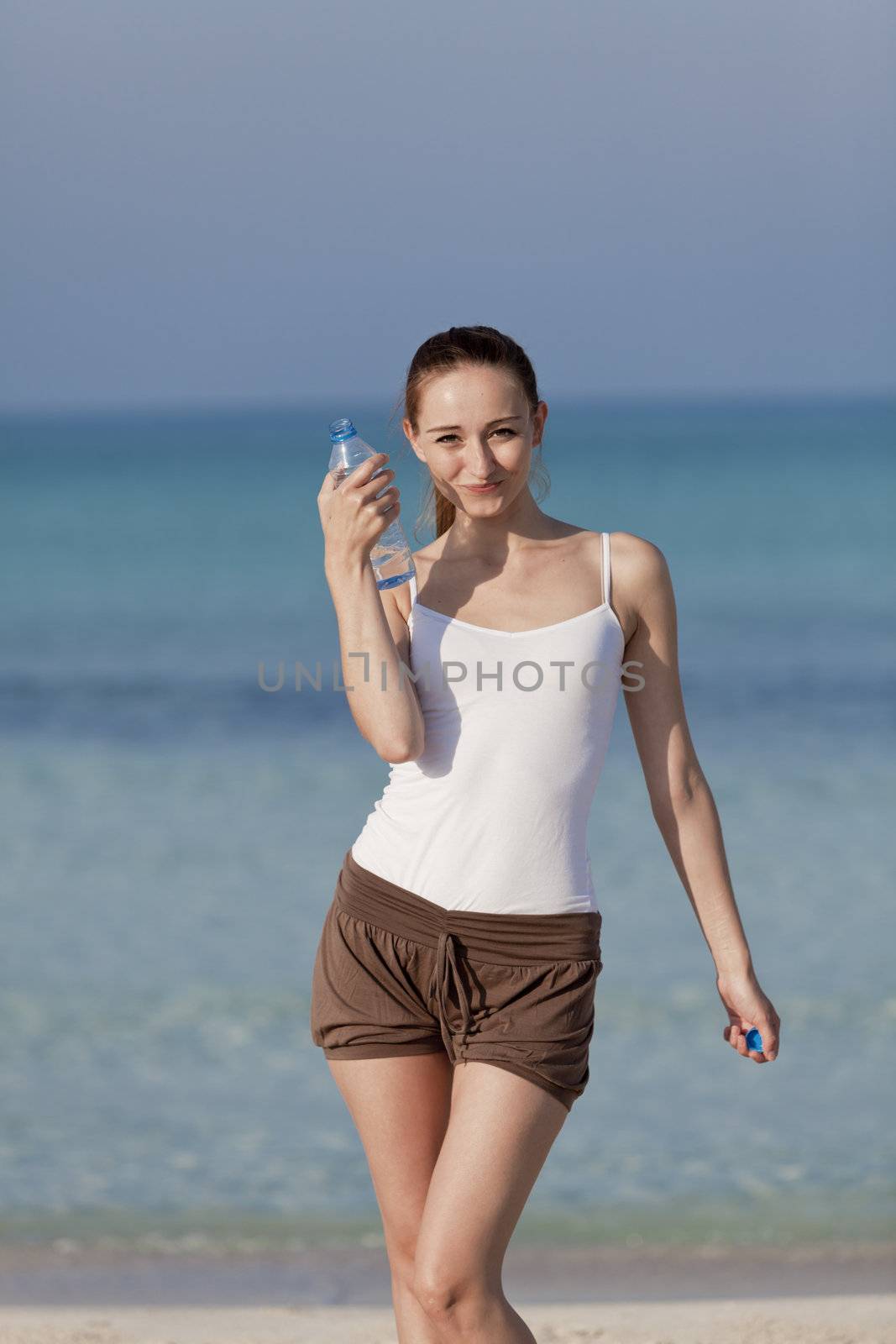 Girl young woman refreshing drinks water from a bottle on the beach by the sea in summer vacation