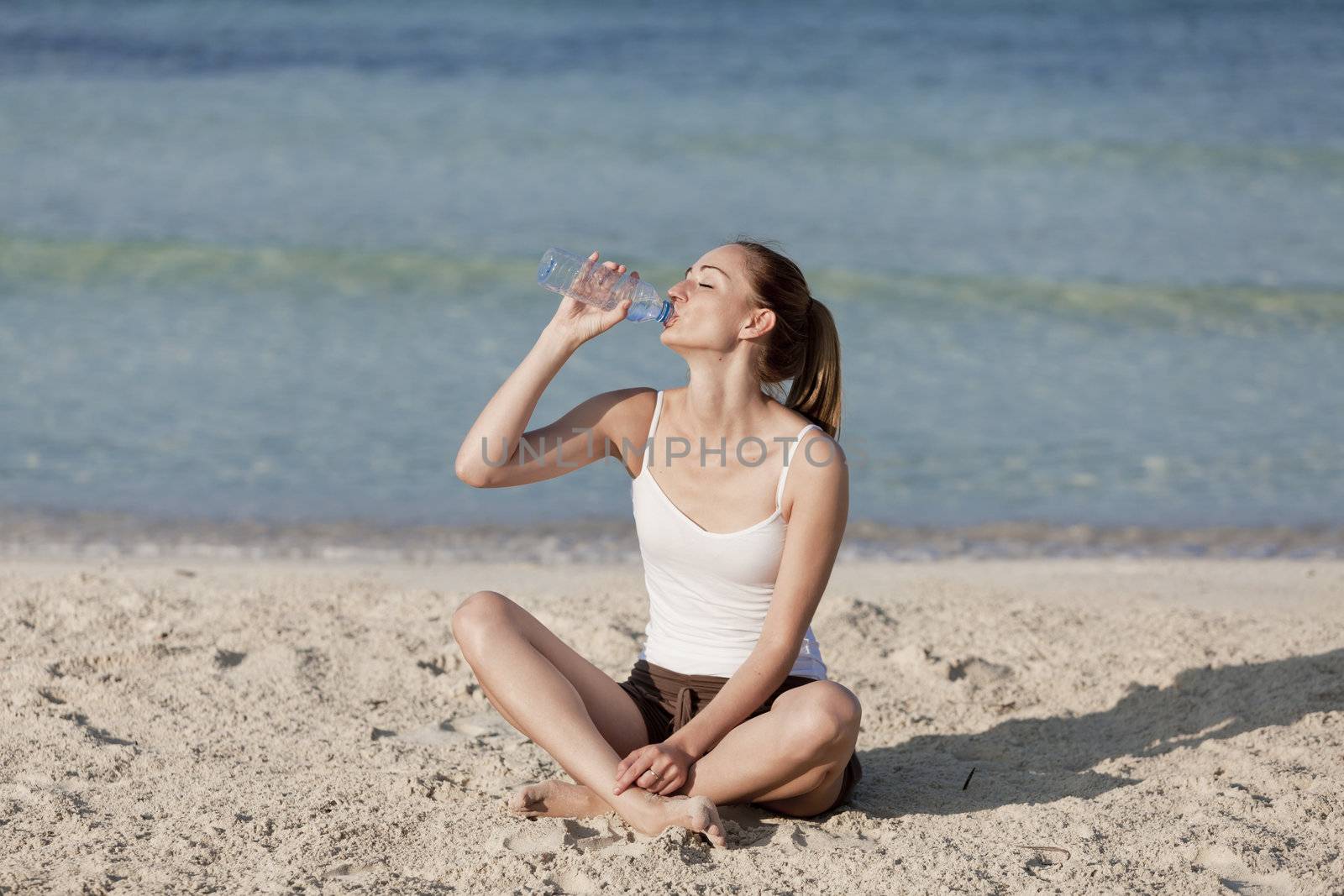 Girl young woman refreshing drinks water from a bottle on the beach by the sea in summer vacation