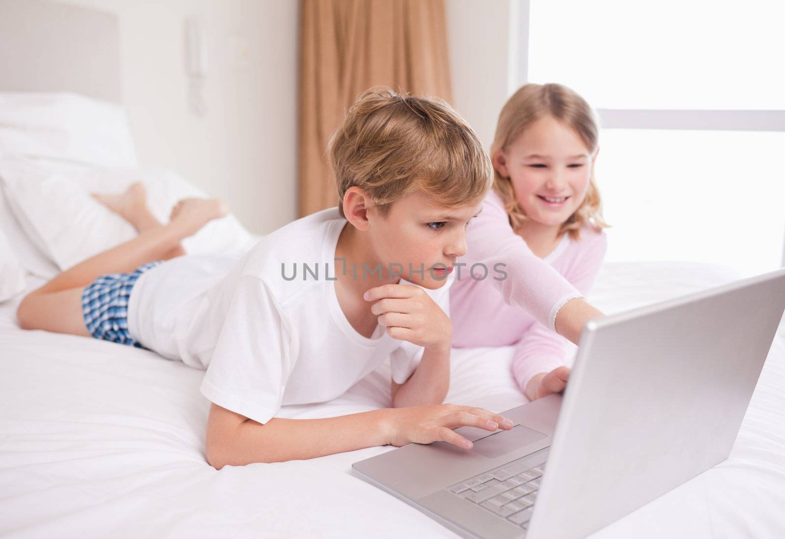 Siblings using a notebook in a bedroom