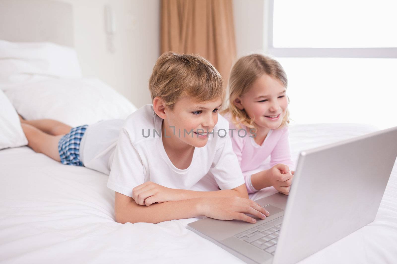 Smiling children using a notebook in a bedroom