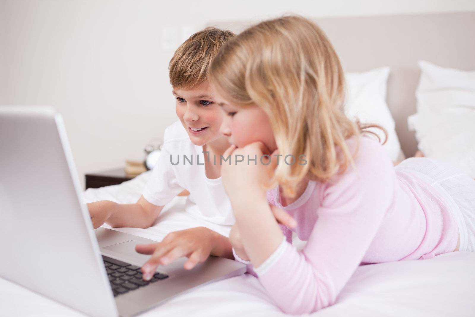 Smiling children using a laptop in a bedroom