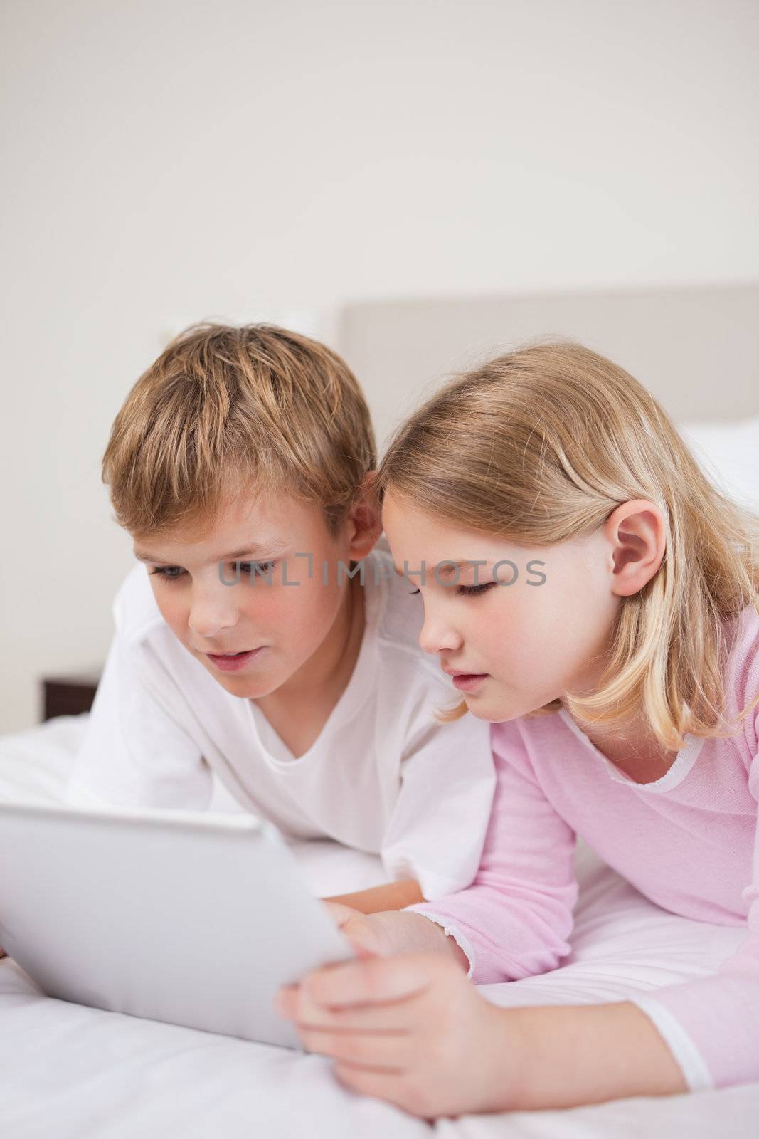 Portrait of cute children using a tablet computer in a bedroom